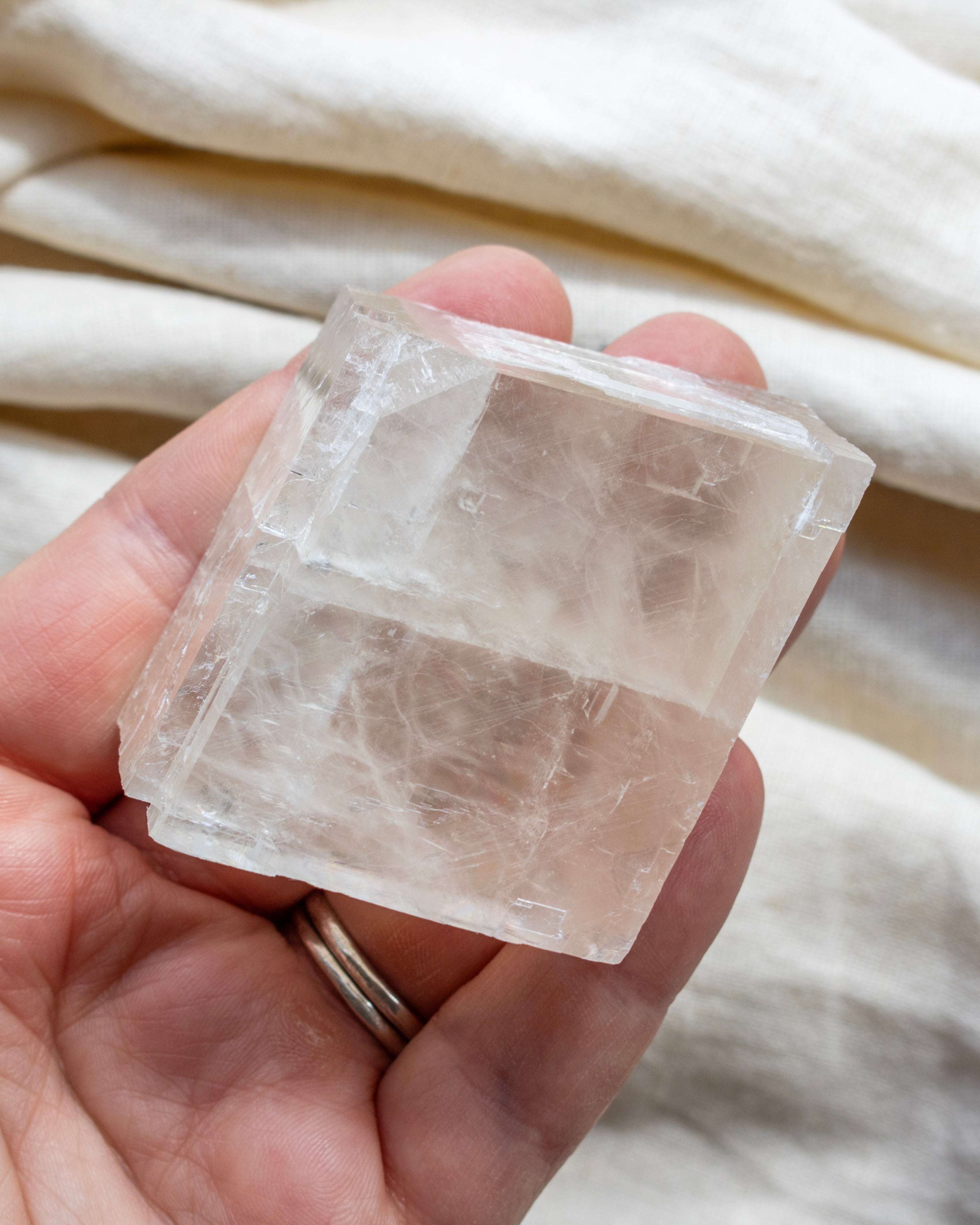 Hand holding a clear crystal block against a neutral fabric background