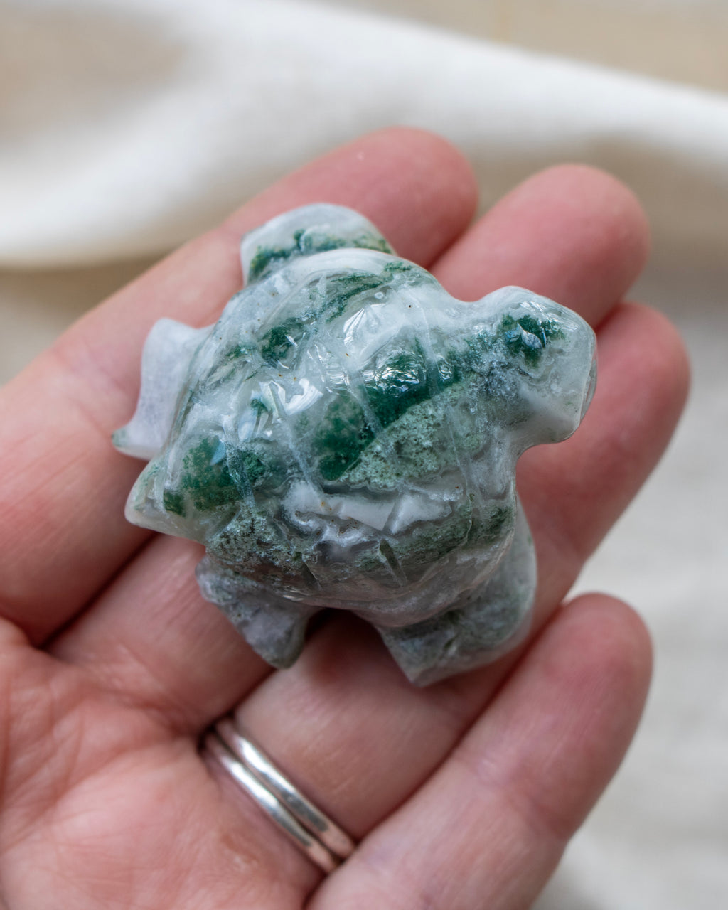 Hand holding a green and white crystal turtle figurine against a neutral background