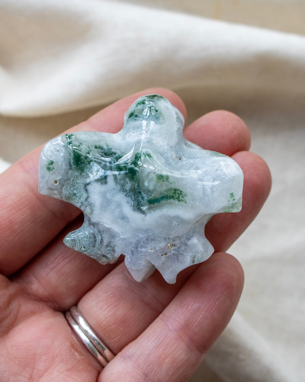 Hand holding a green and white crystal rock against a neutral background
