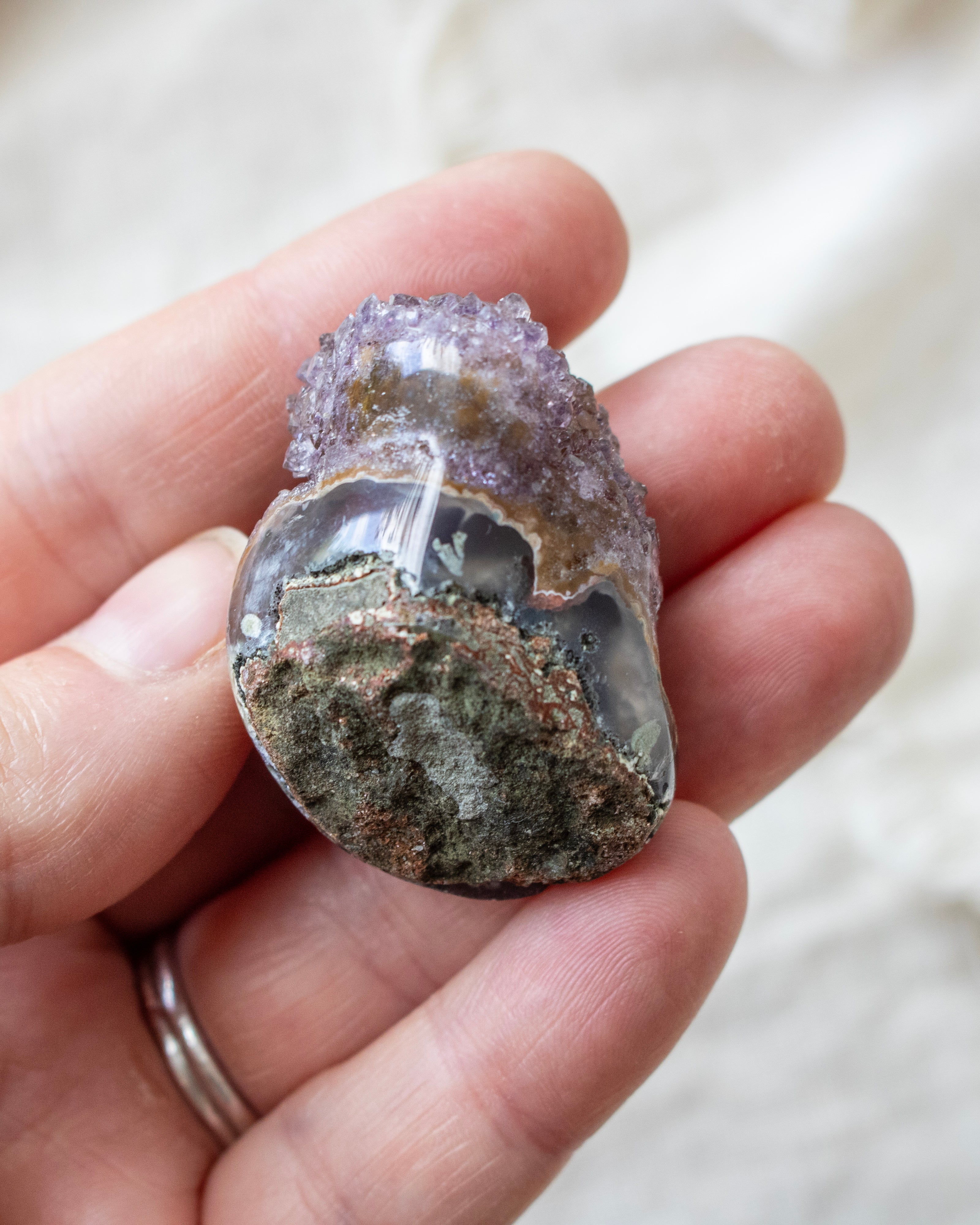 Hand holding a geode with amethyst crystals against a neutral background