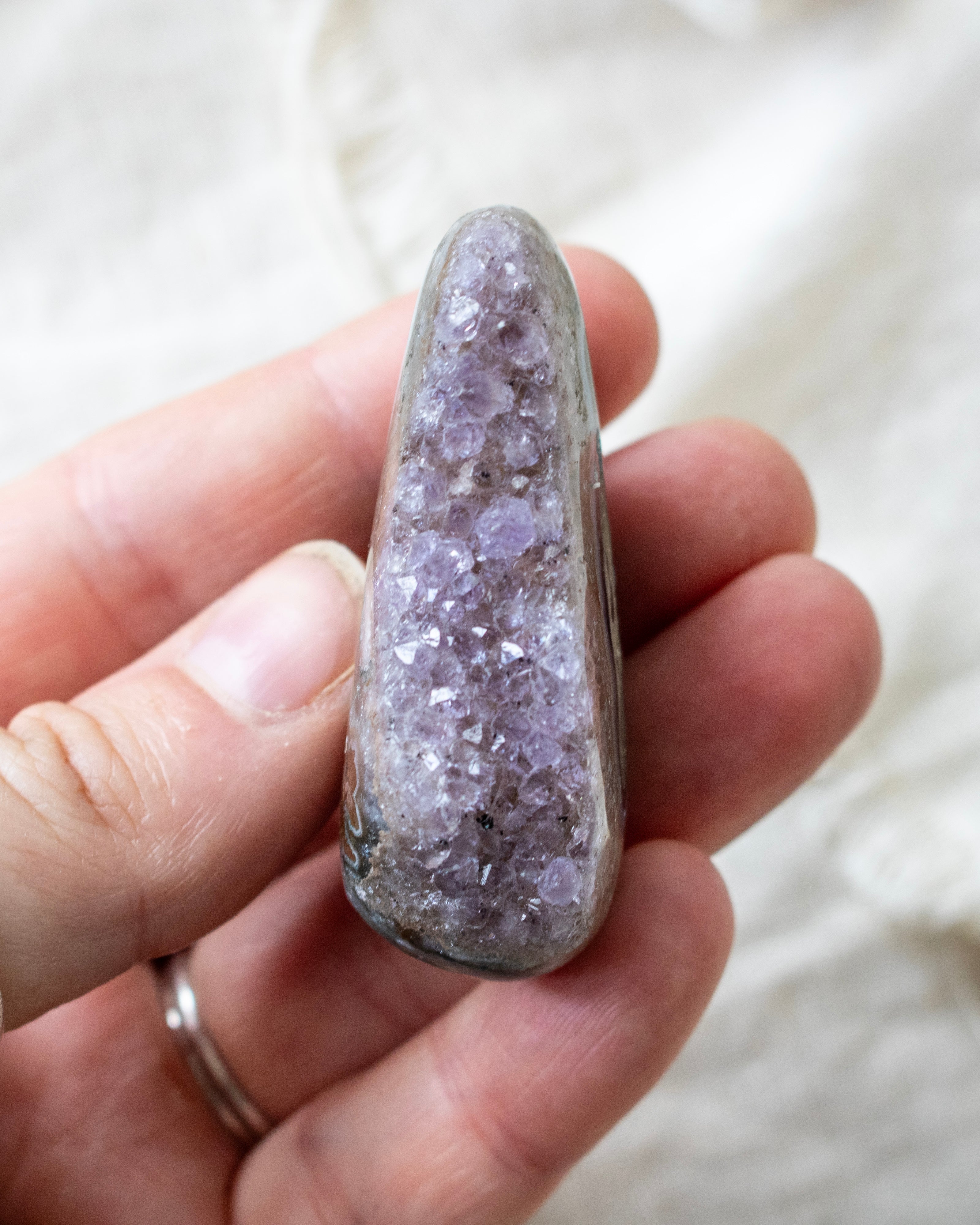 Hand holding a crystal with purple and white coloration against a neutral background