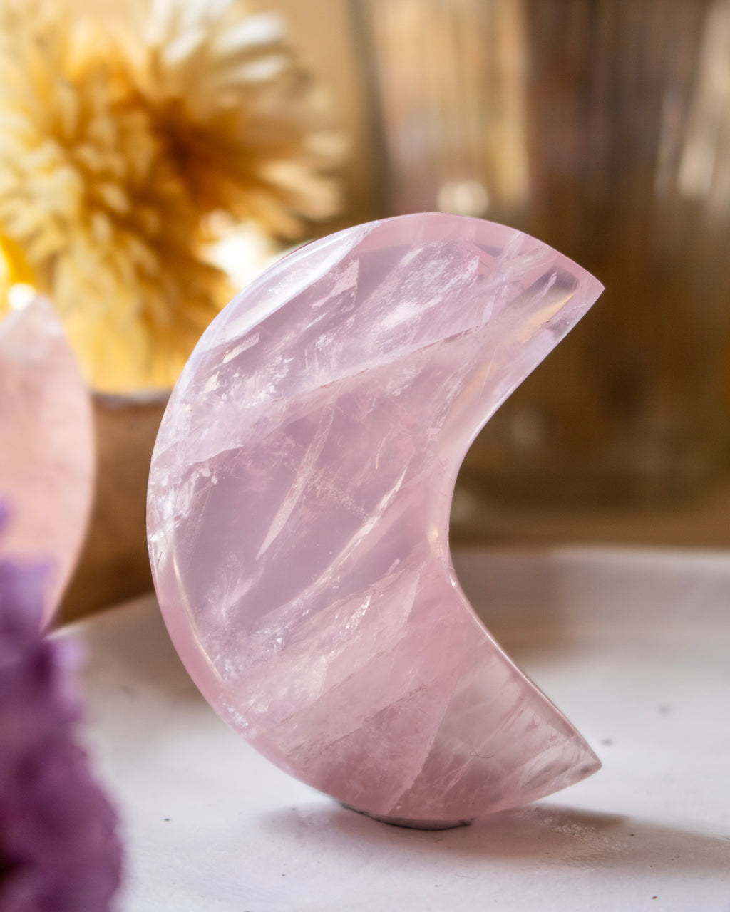 Pink crystal moon shape on a white surface with blurred background