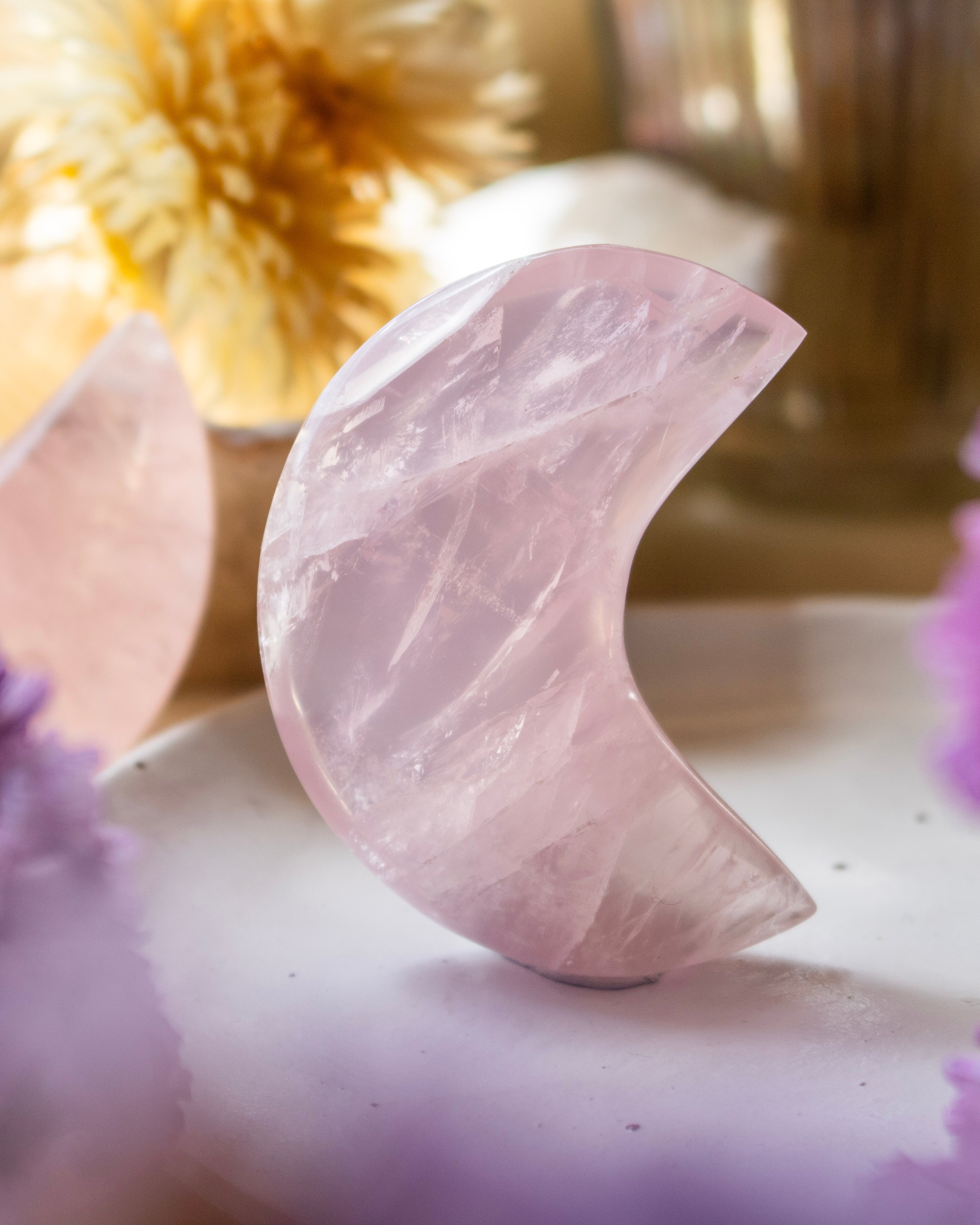 Pink crystal half-moon shape on a white surface with blurred decorative background