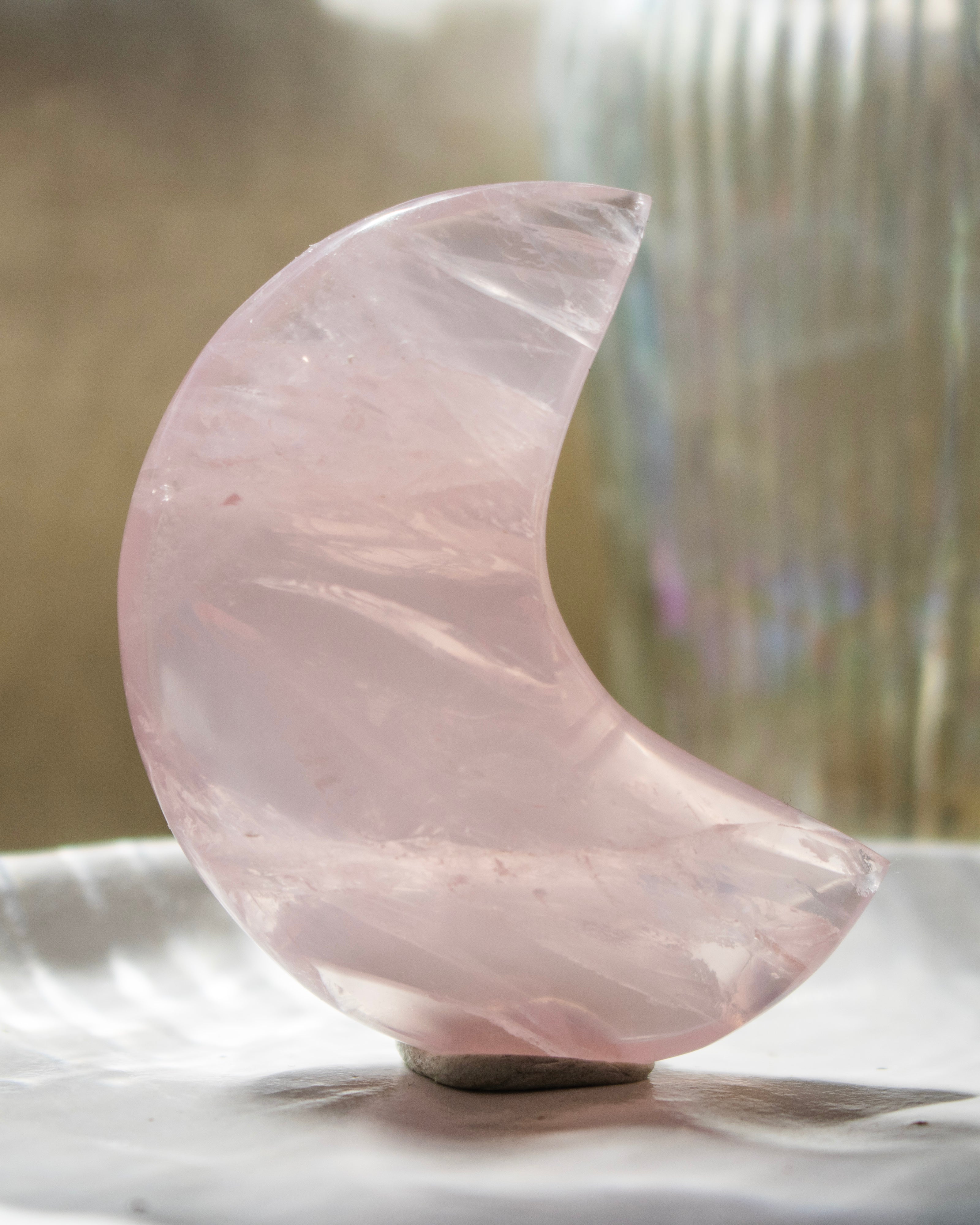Rose quartz crystal in the shape of a crescent moon on a white surface with a blurred background