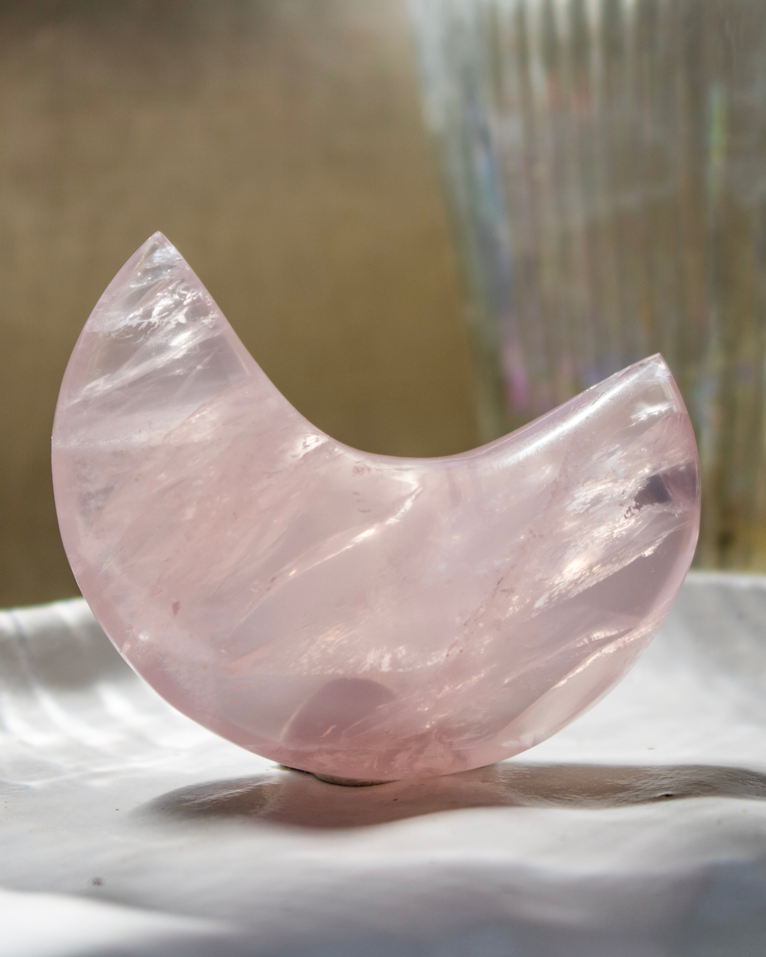 Pink crystal moon shape on a reflective surface with a blurred background