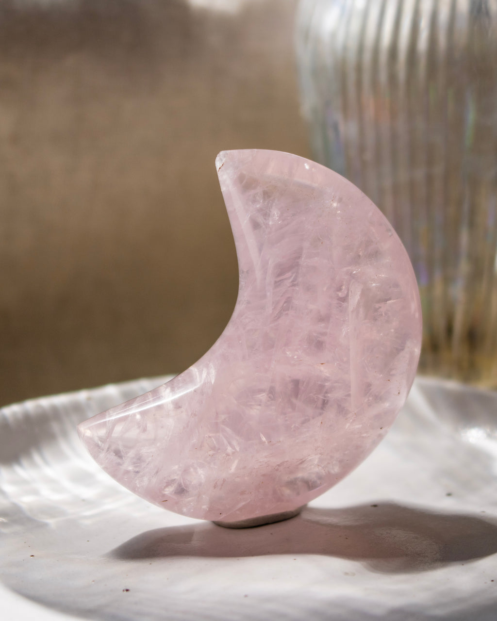 Pink crystal crescent moon on a reflective surface with a blurred background