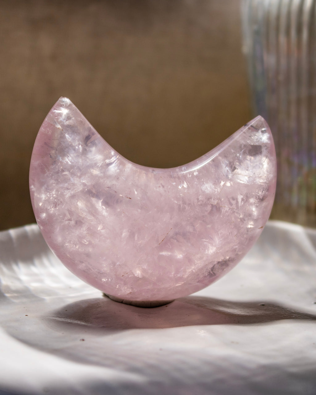 Pink crystal half-moon shape on a textured surface with a blurred background