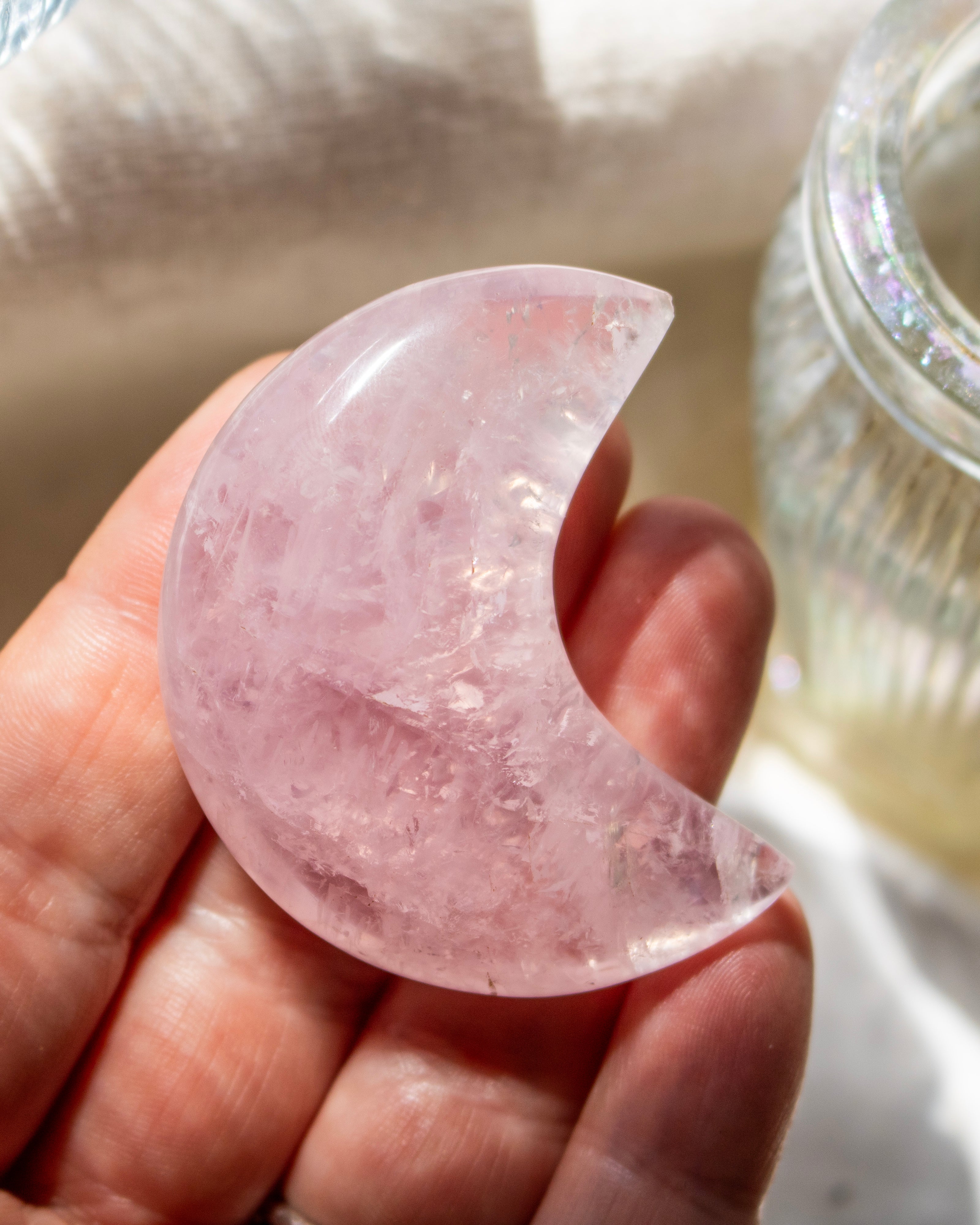 Pink crystal crescent moon held in a hand with a blurred background