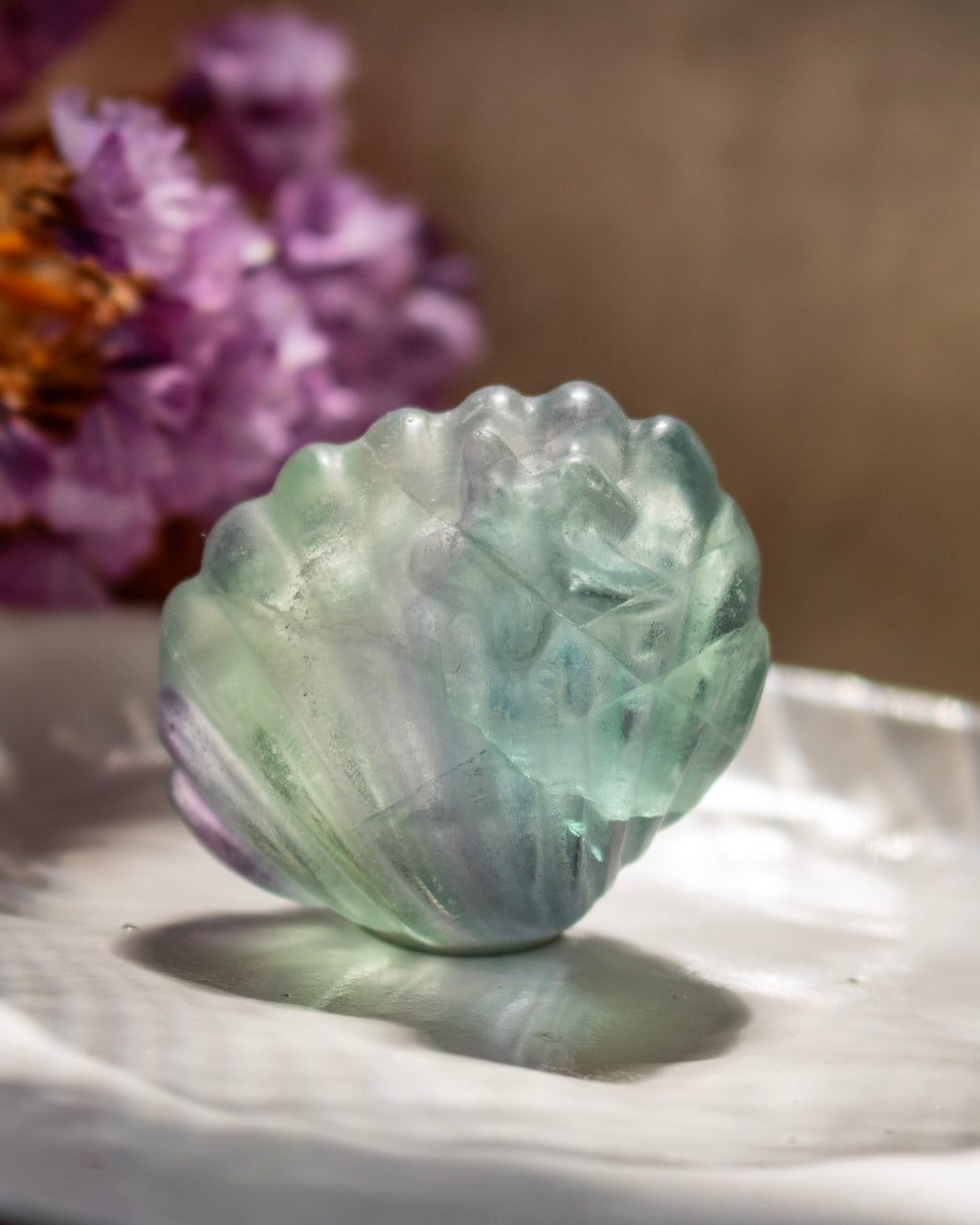 Green crystal on a white surface with purple flowers in the background