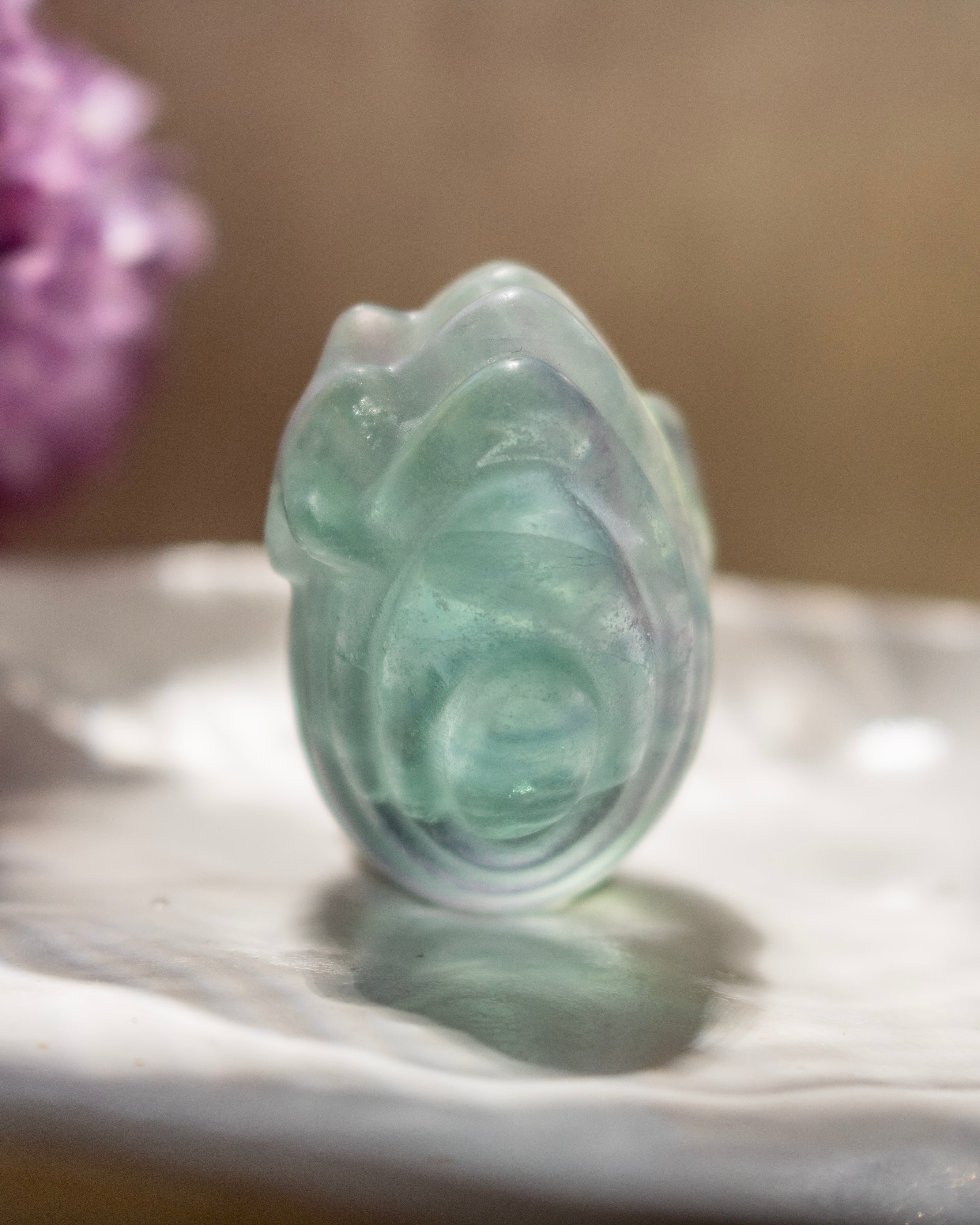 Translucent green jade carving on a marble surface with a blurred background