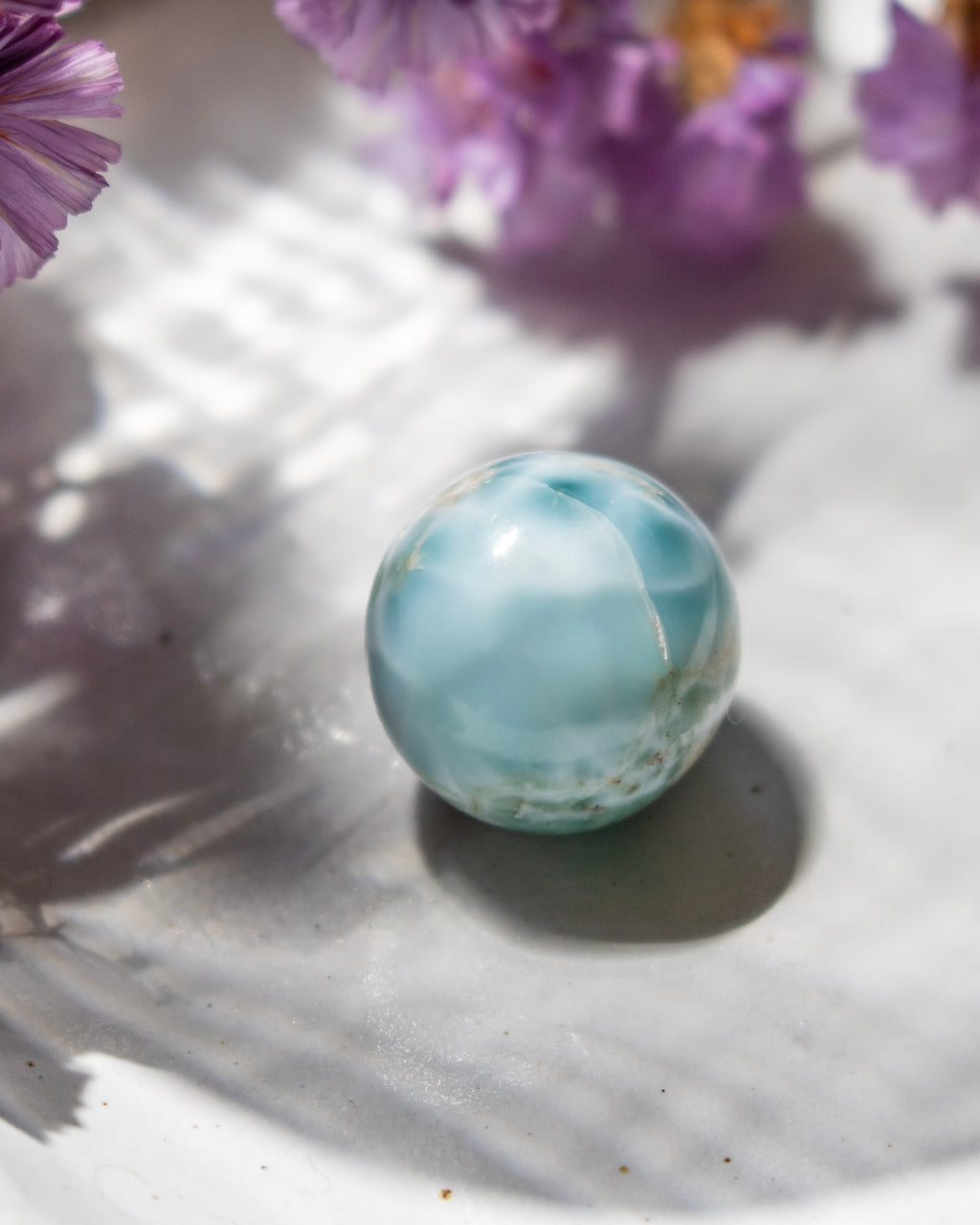 Marbled blue and white sphere on a light surface with purple flowers in the background