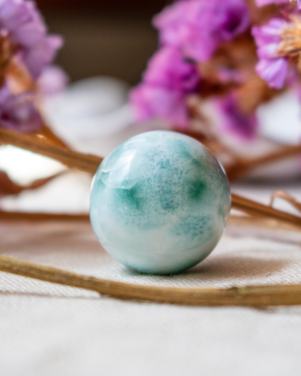 Green sphere on a textured surface with blurred purple flowers in the background