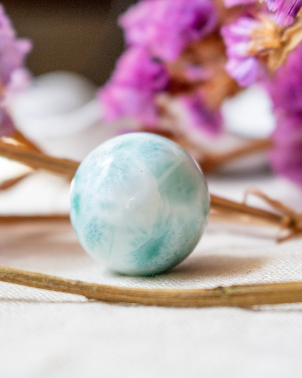 Marbled blue and white sphere on a textured surface with blurred pink flowers in the background