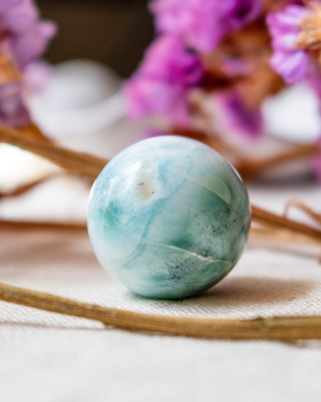 Marble-textured sphere on a textured surface with blurred purple flowers in the background