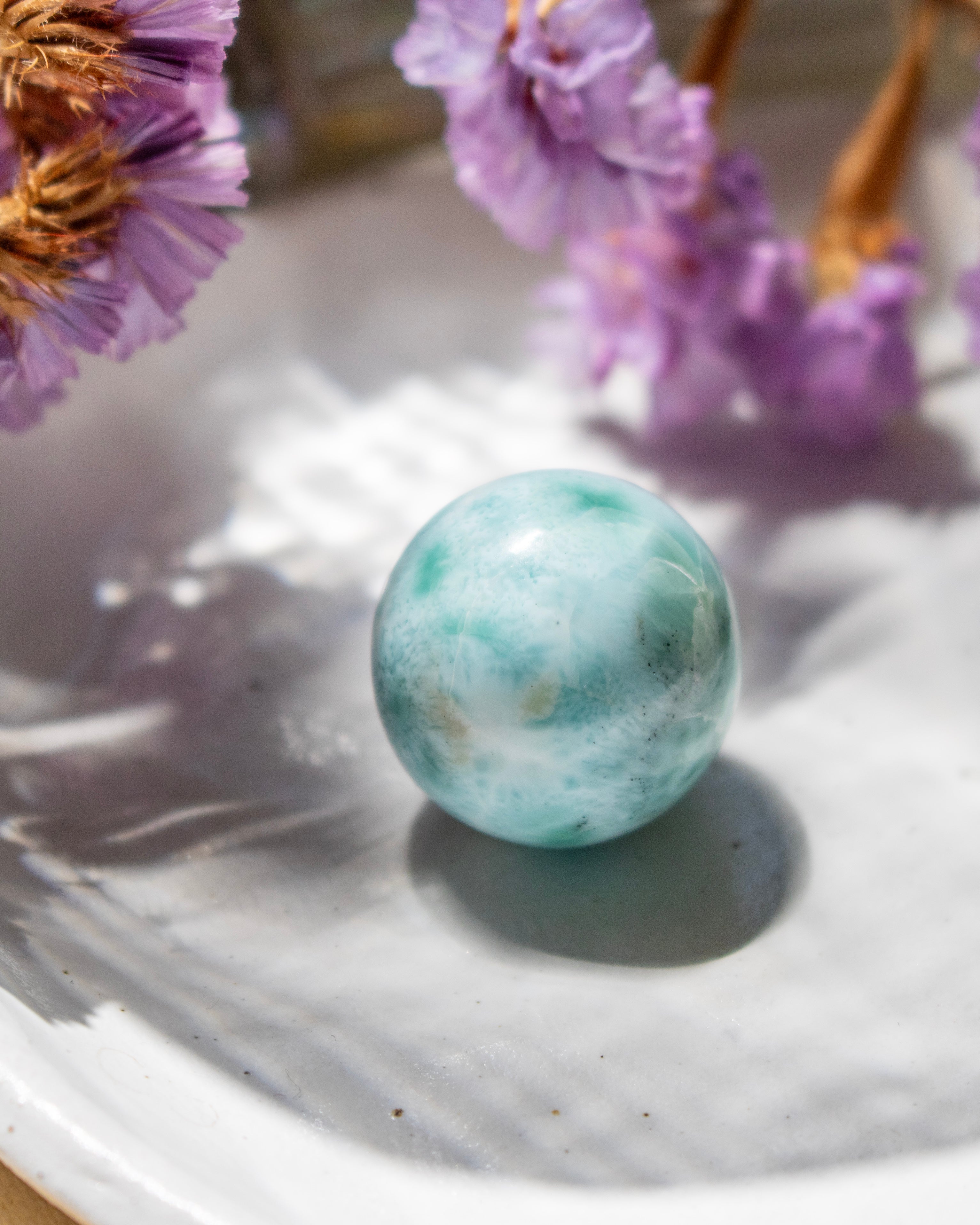 Turquoise marble on a white surface with purple flowers in the background