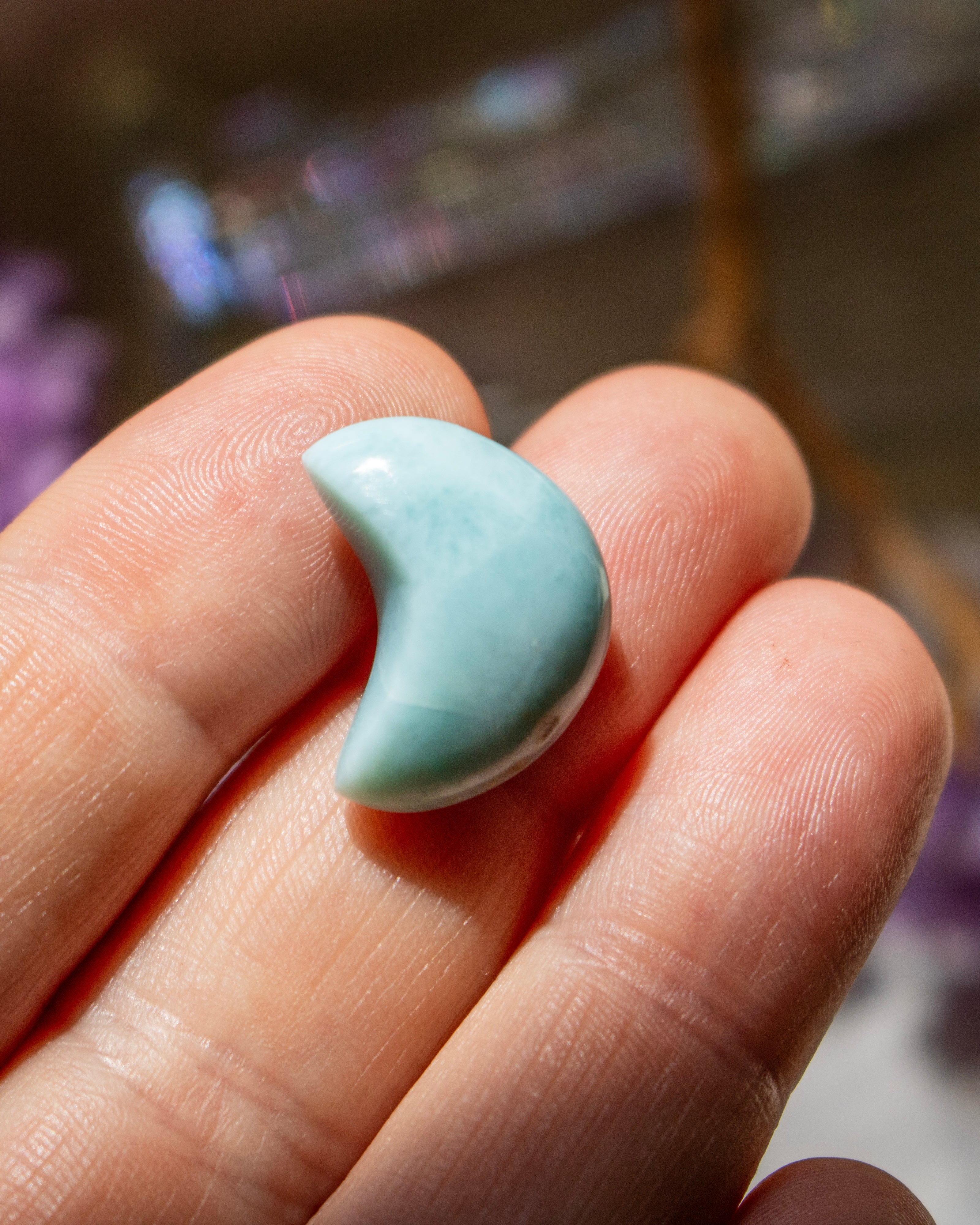 Turquoise larimar crescent moon on a person's finger with a blurred background