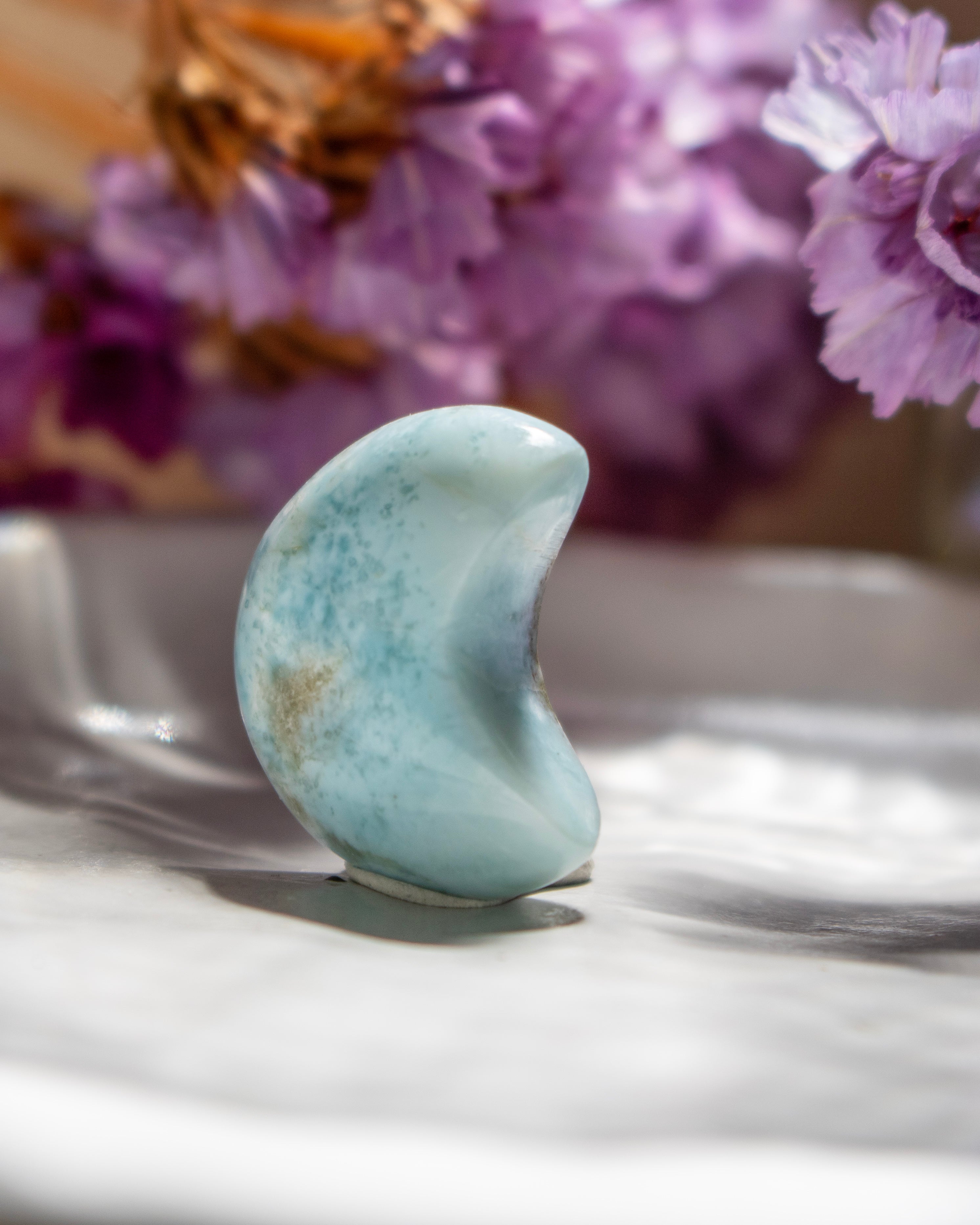 Turquoise stone on a reflective surface with purple flowers in the background