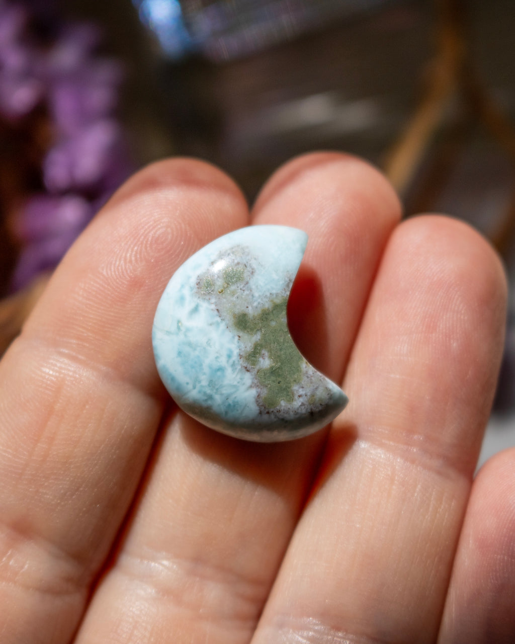 Half-moon shaped turquoise stone held between fingers with a blurred background