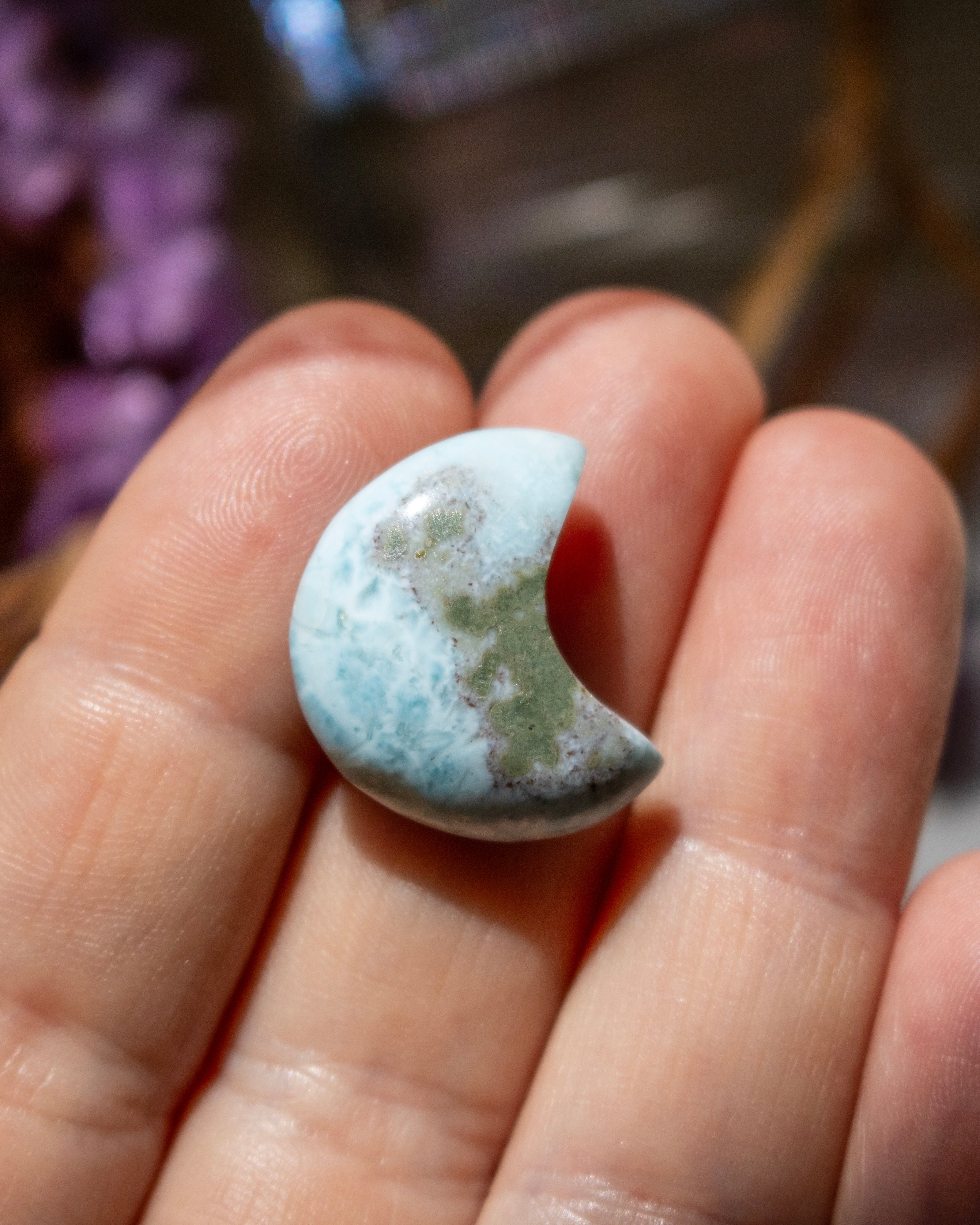 Half-moon shaped turquoise stone held between fingers with a blurred background