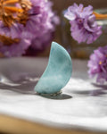 Teal stone sculpture on a marble surface with blurred purple flowers in the background