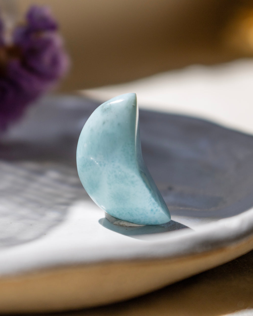 Blue stone shaped like a crescent moon on a white plate with a blurred background