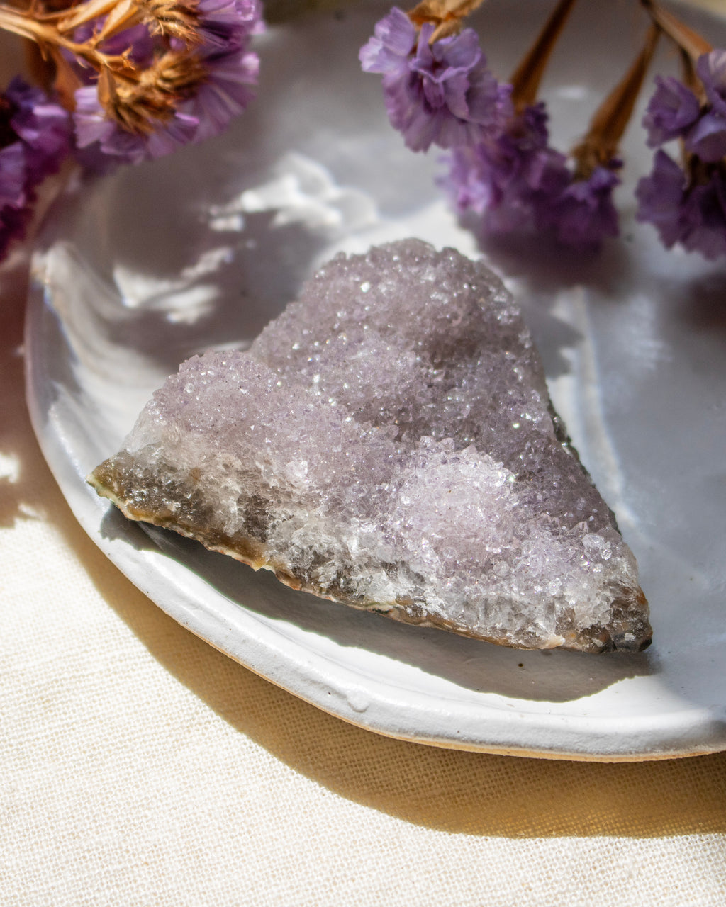 Geode crystal on a white plate with purple flowers in the background