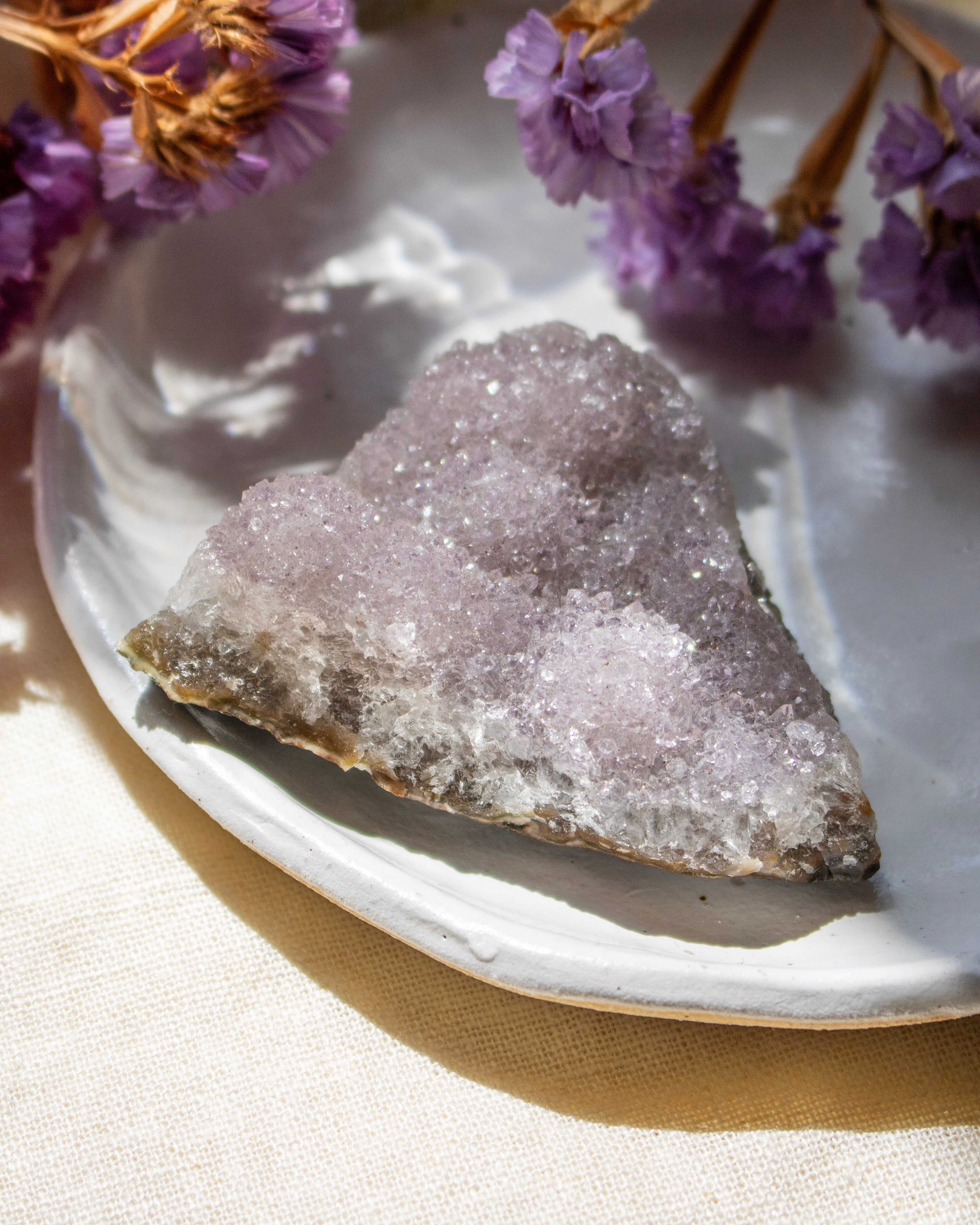 Geode crystal on a white plate with purple flowers in the background