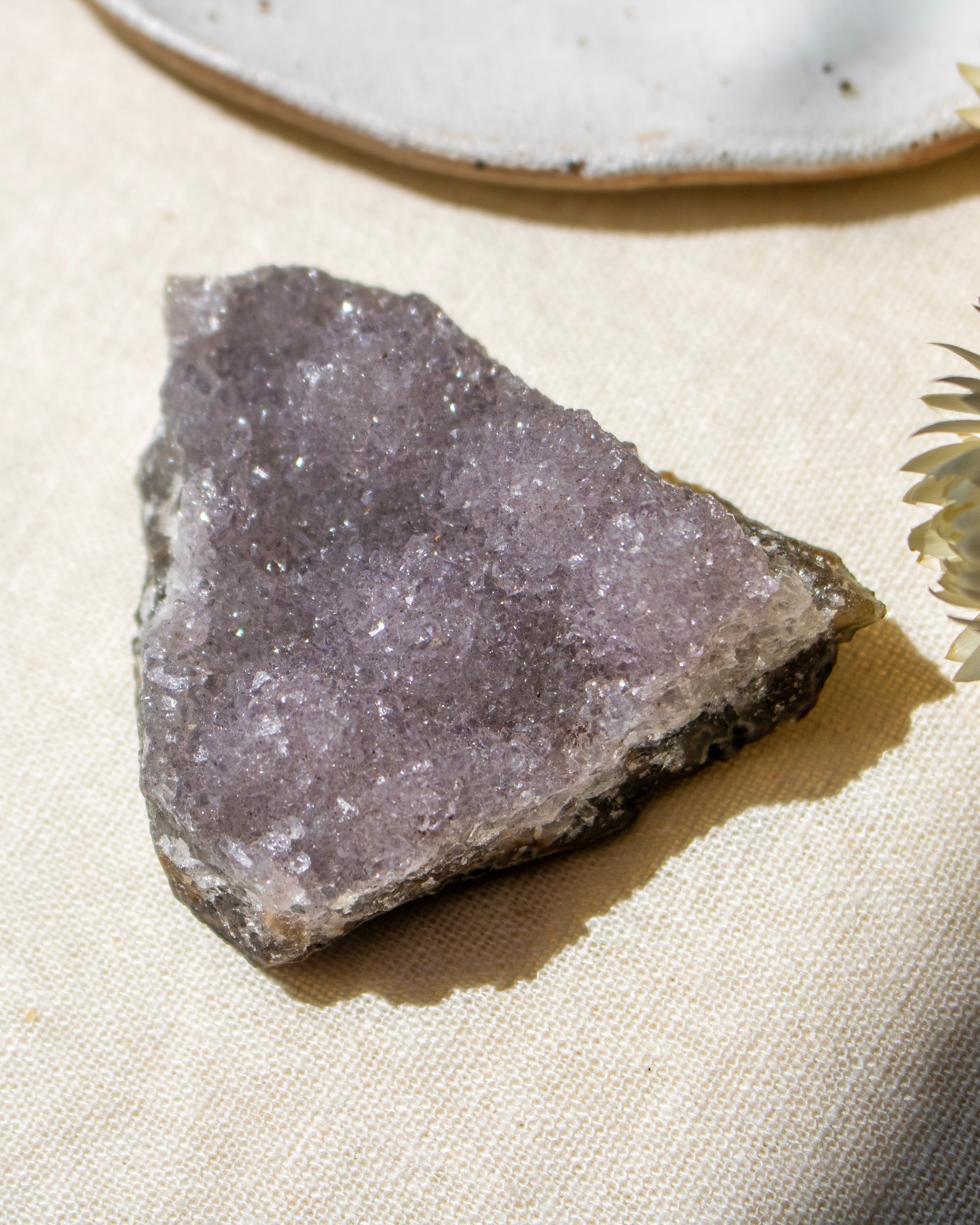 Raw amethyst crystal on a beige surface with a ceramic plate in the background