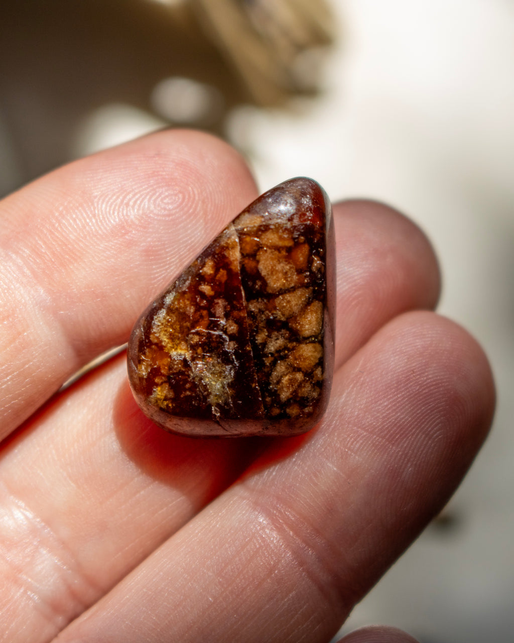 Brown gemstone held between fingers against a blurred background