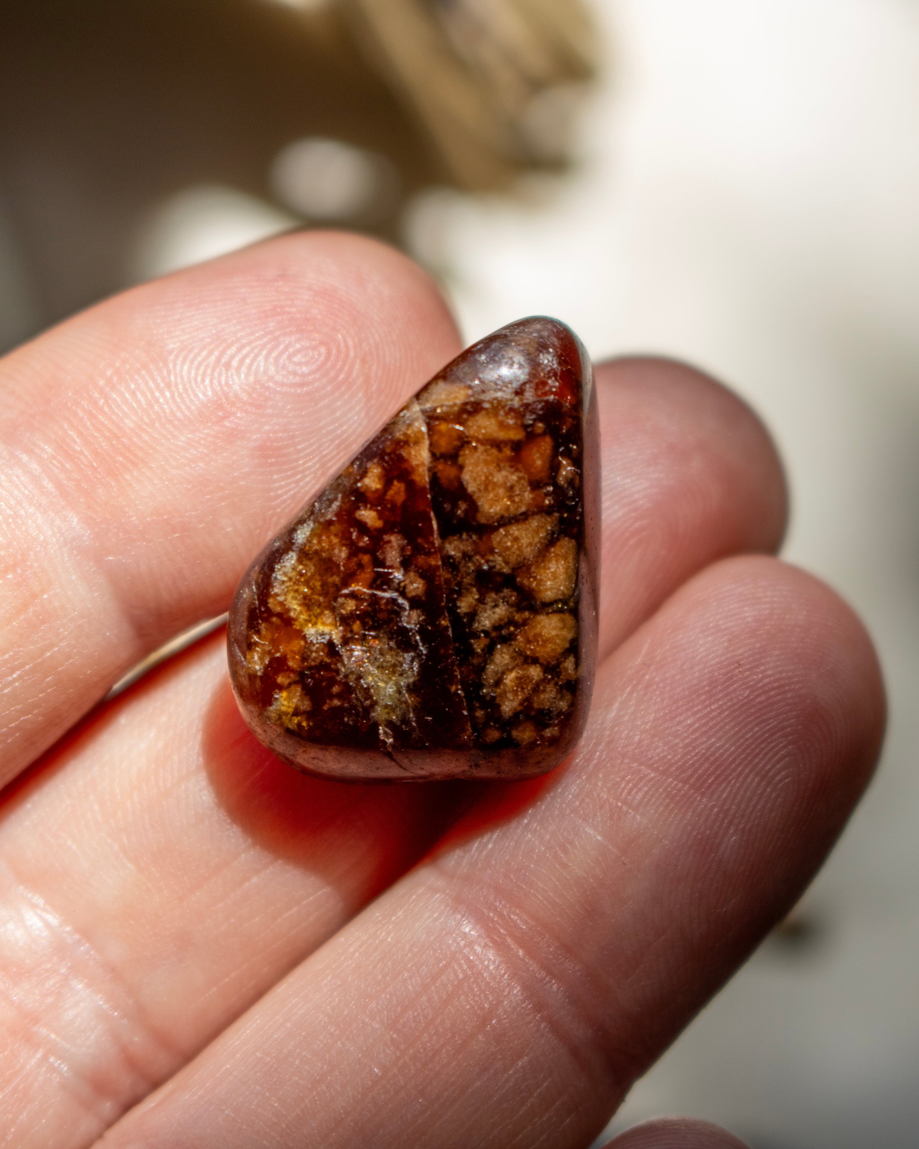 Brown gemstone held between fingers against a blurred background