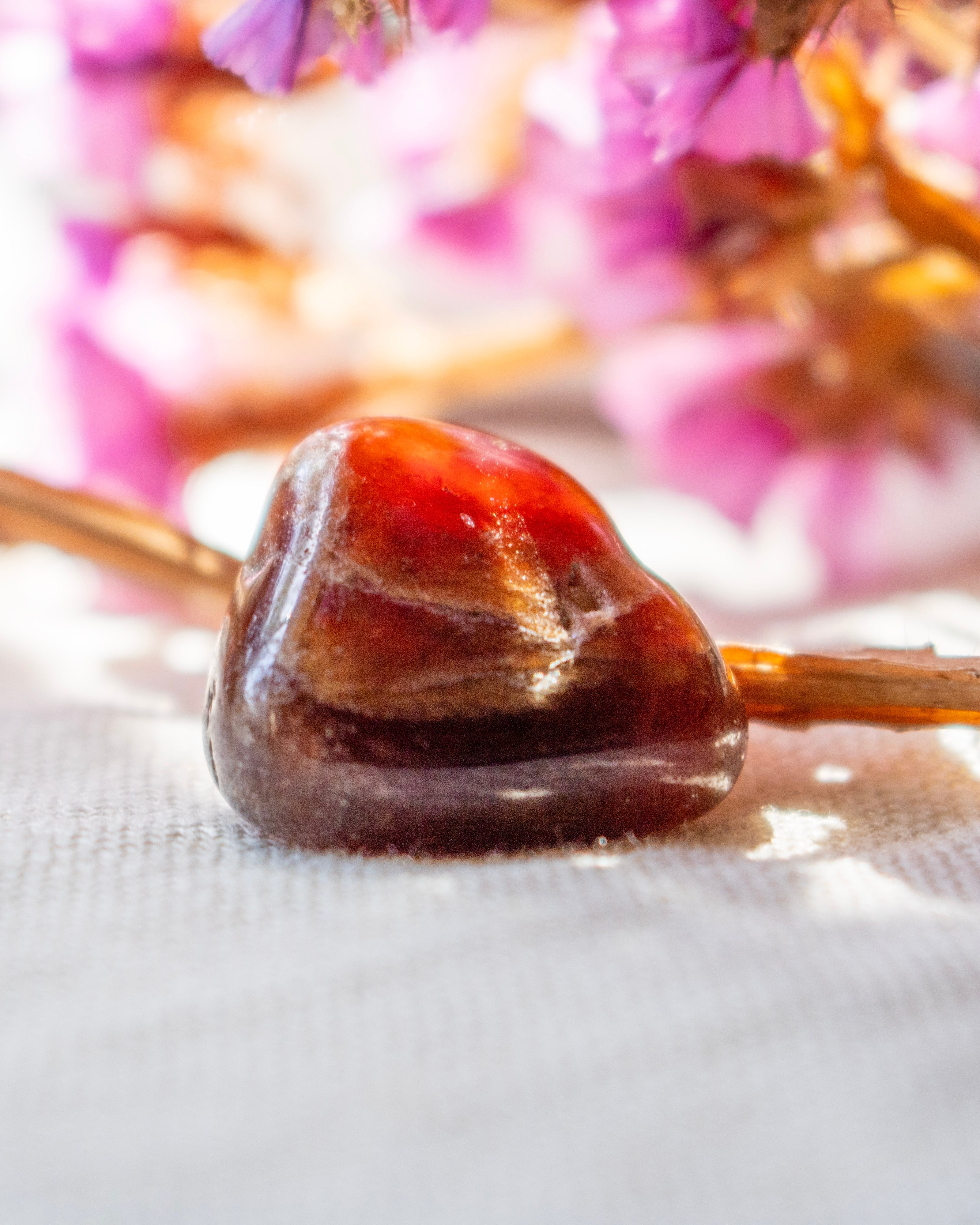 Close-up of a polished brown stone on a white surface with blurred pink flowers in the background