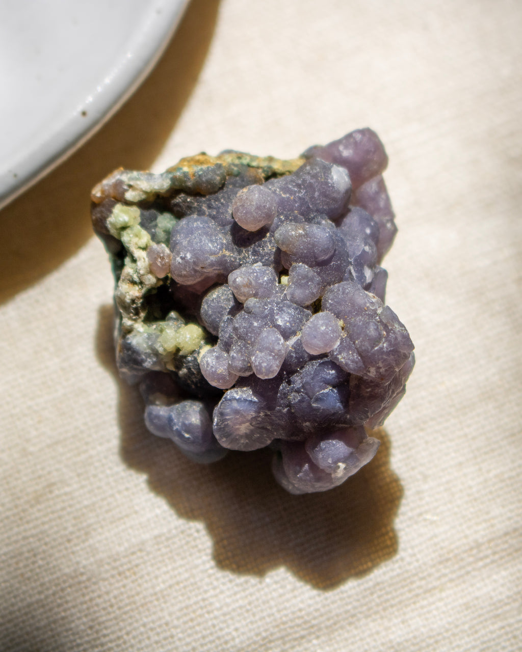 Close-up of a purple crystal on a reflective surface with blurred purple flowers in the background.