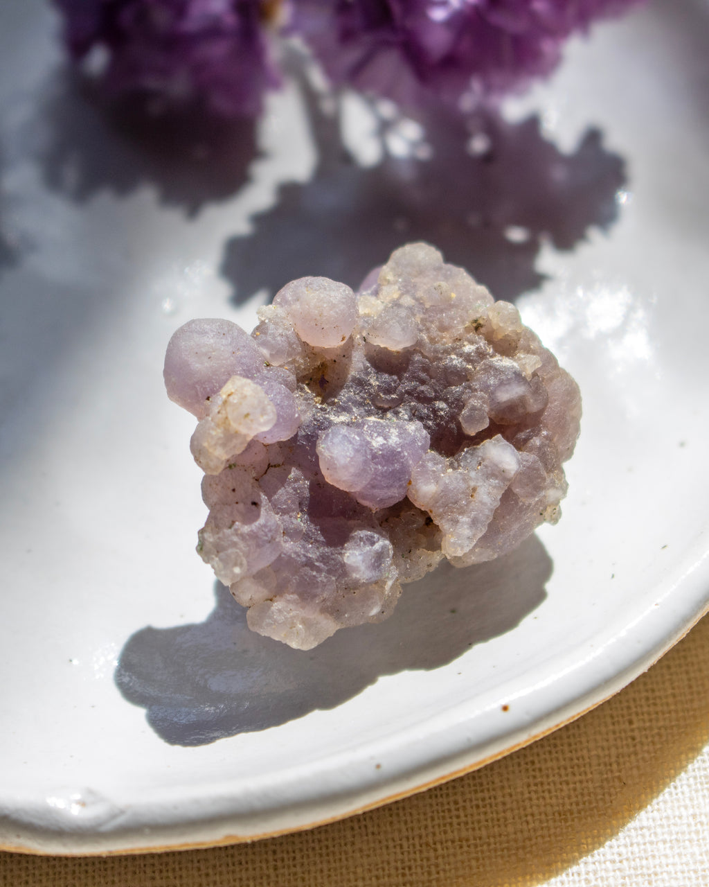 Purple crystal cluster on a white plate with a blurred background