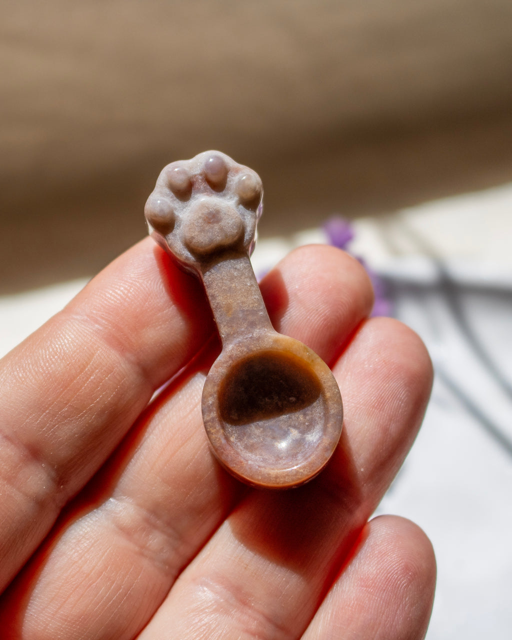 A small carved spoon-shaped object with a paw-print handle, held in a person's hand against a softly blurred beige background.