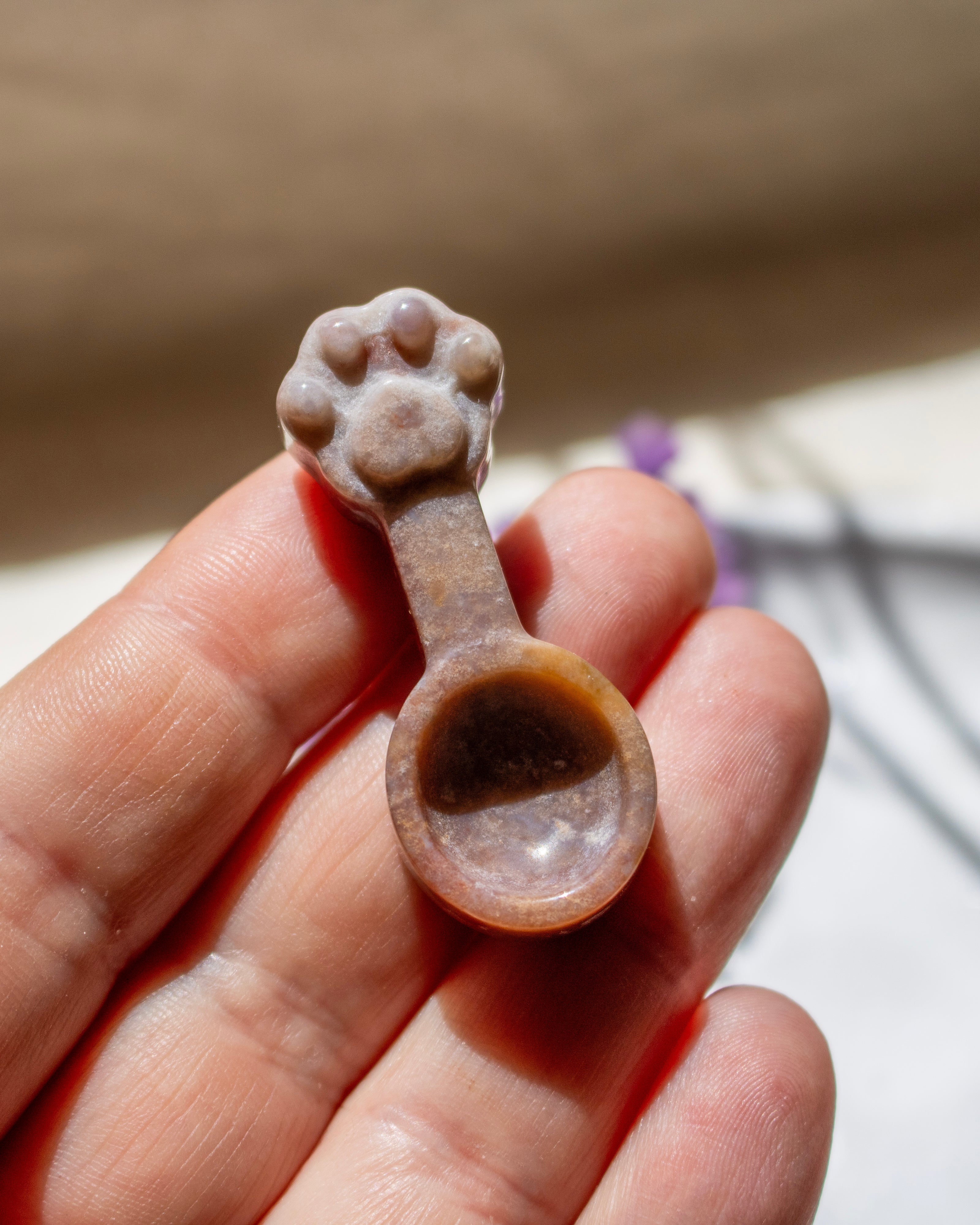 A small carved spoon-shaped object with a paw-print handle, held in a person's hand against a softly blurred beige background.
