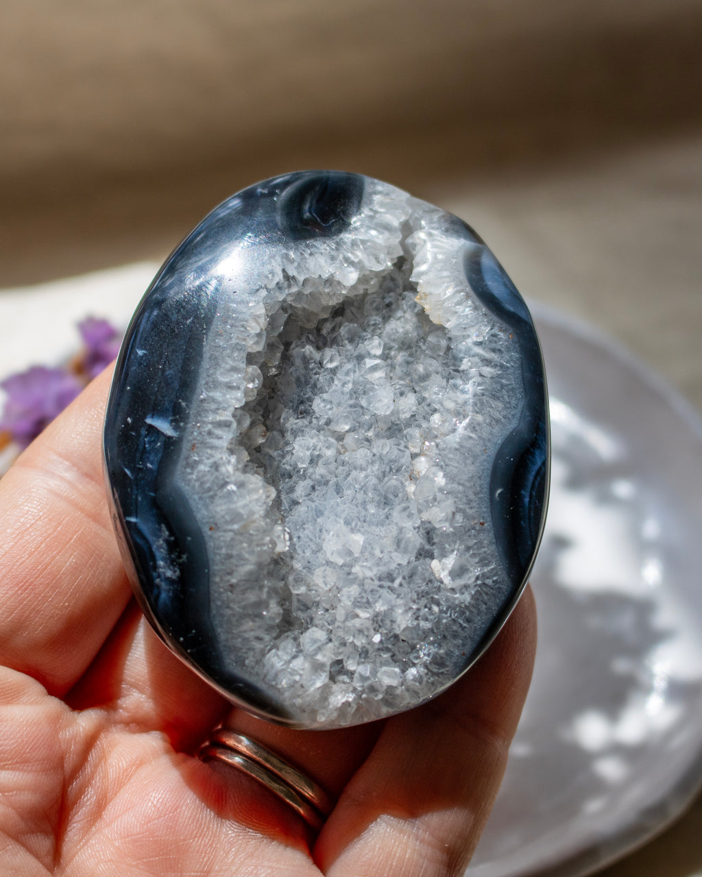 A polished geode specimen with a dark blue outer border and a white crystal cavity, held in a person's hand.