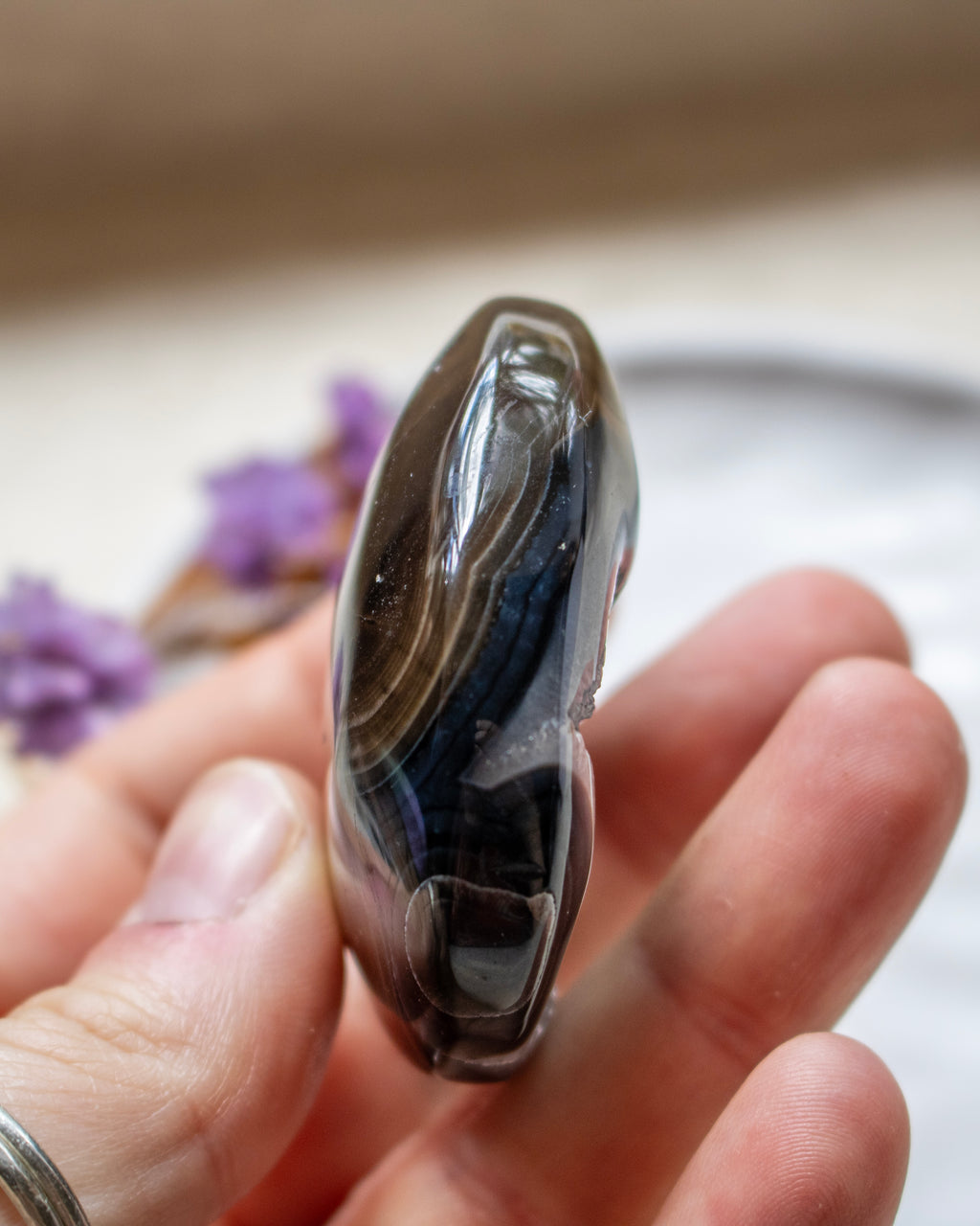 A polished dark agate stone with black, gray, and brown banding, held in a person's hand.