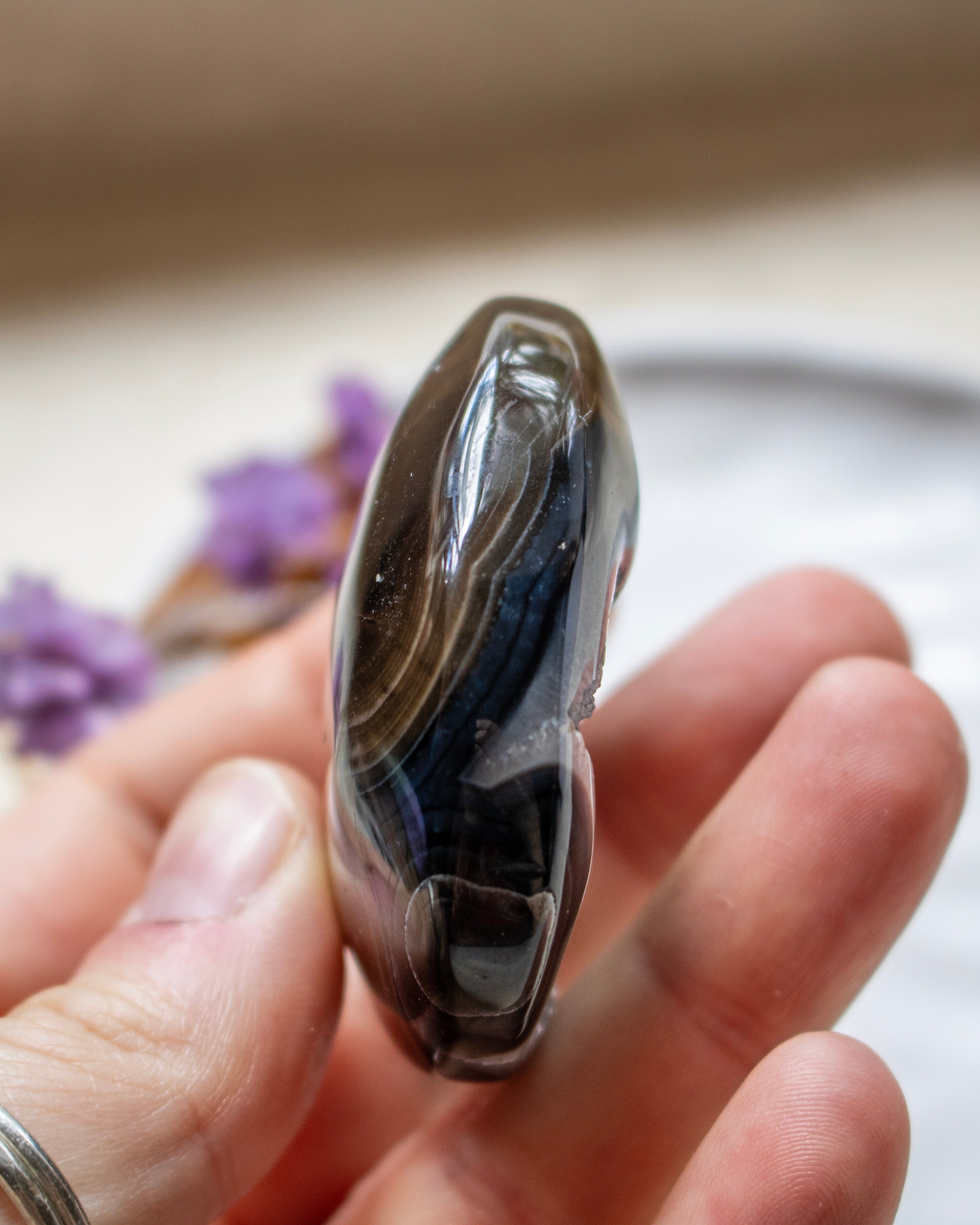 A polished dark agate stone with black, gray, and brown banding, held in a person's hand.