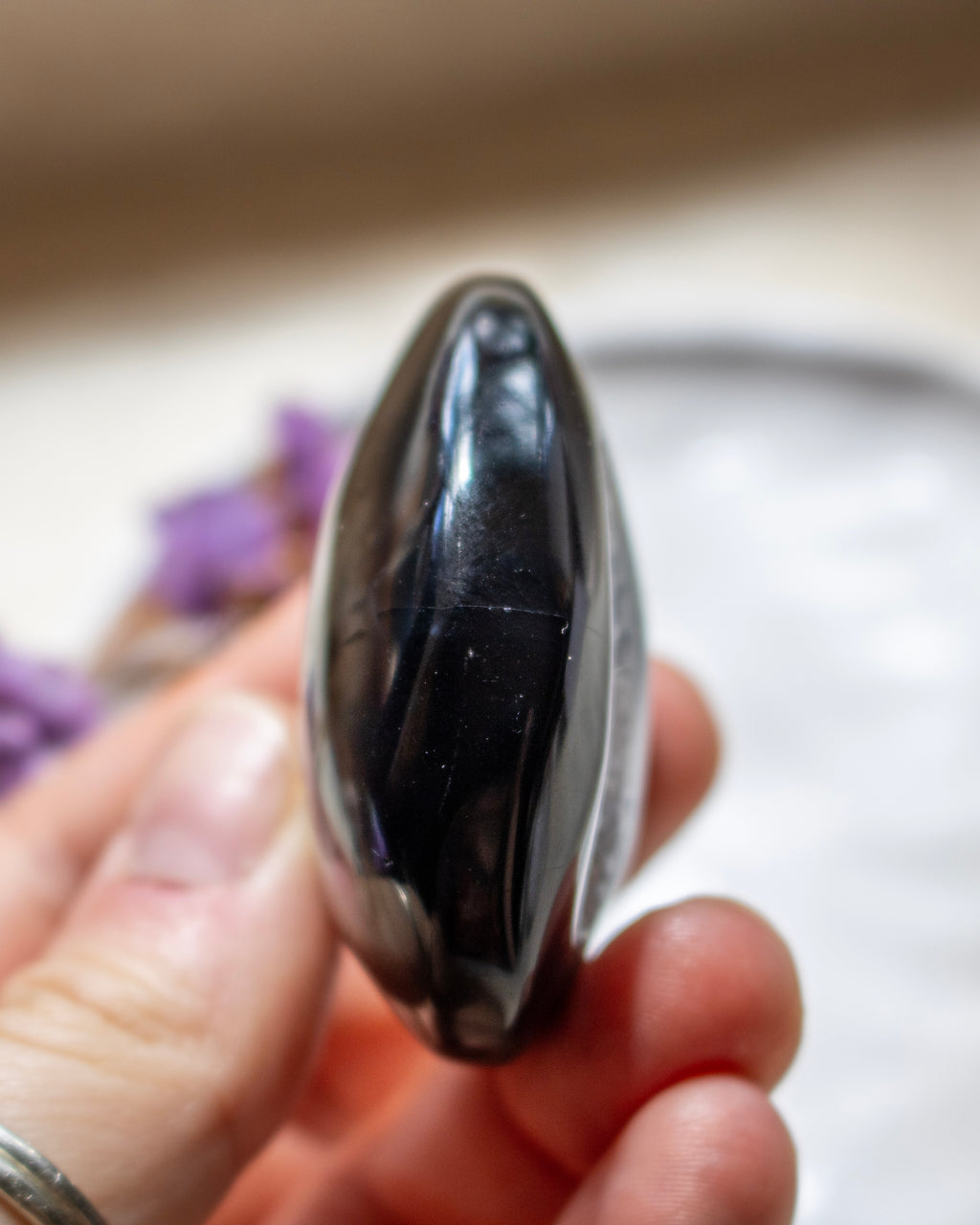 A polished black agate teardrop-shaped crystal held in a person's hand, showing a glossy, reflective surface with natural inclusions.