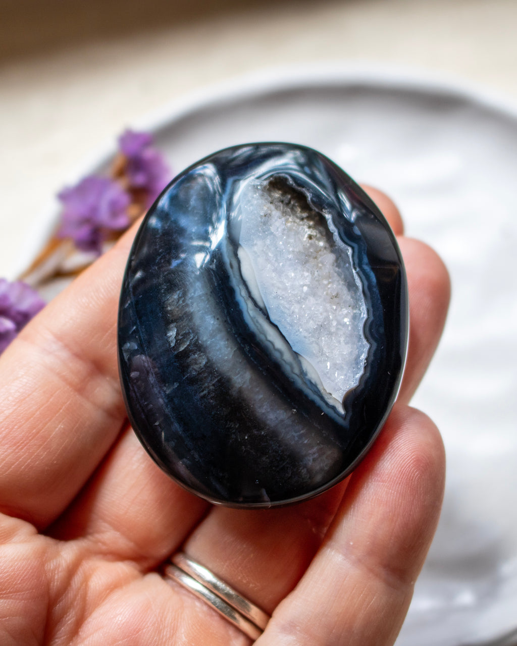 A polished oval black stone with a white geode cavity, held in a person's hand.