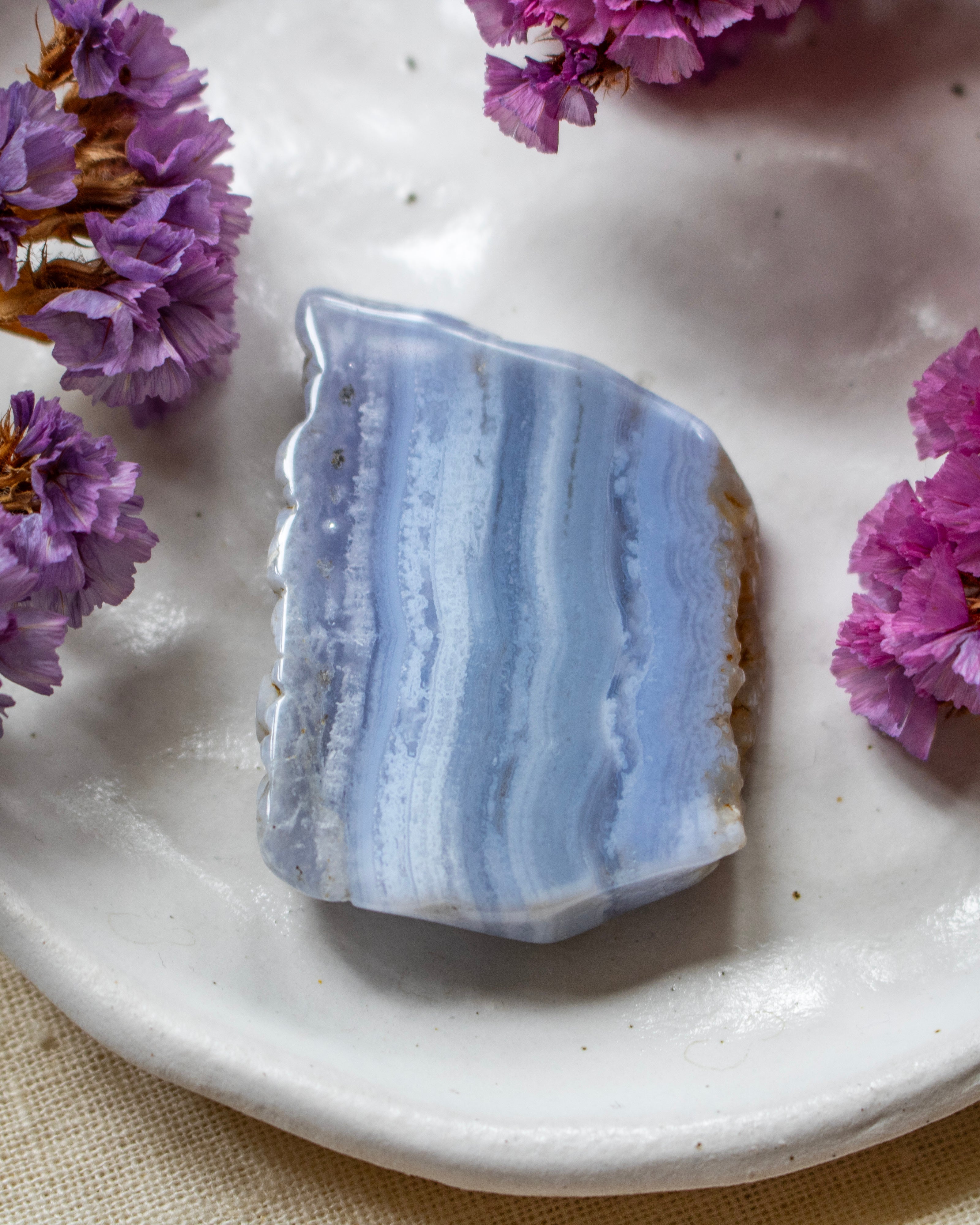 A polished blue and white banded stone slab, resembling agate or marble, displayed on a white ceramic plate with small purple flowers around it.