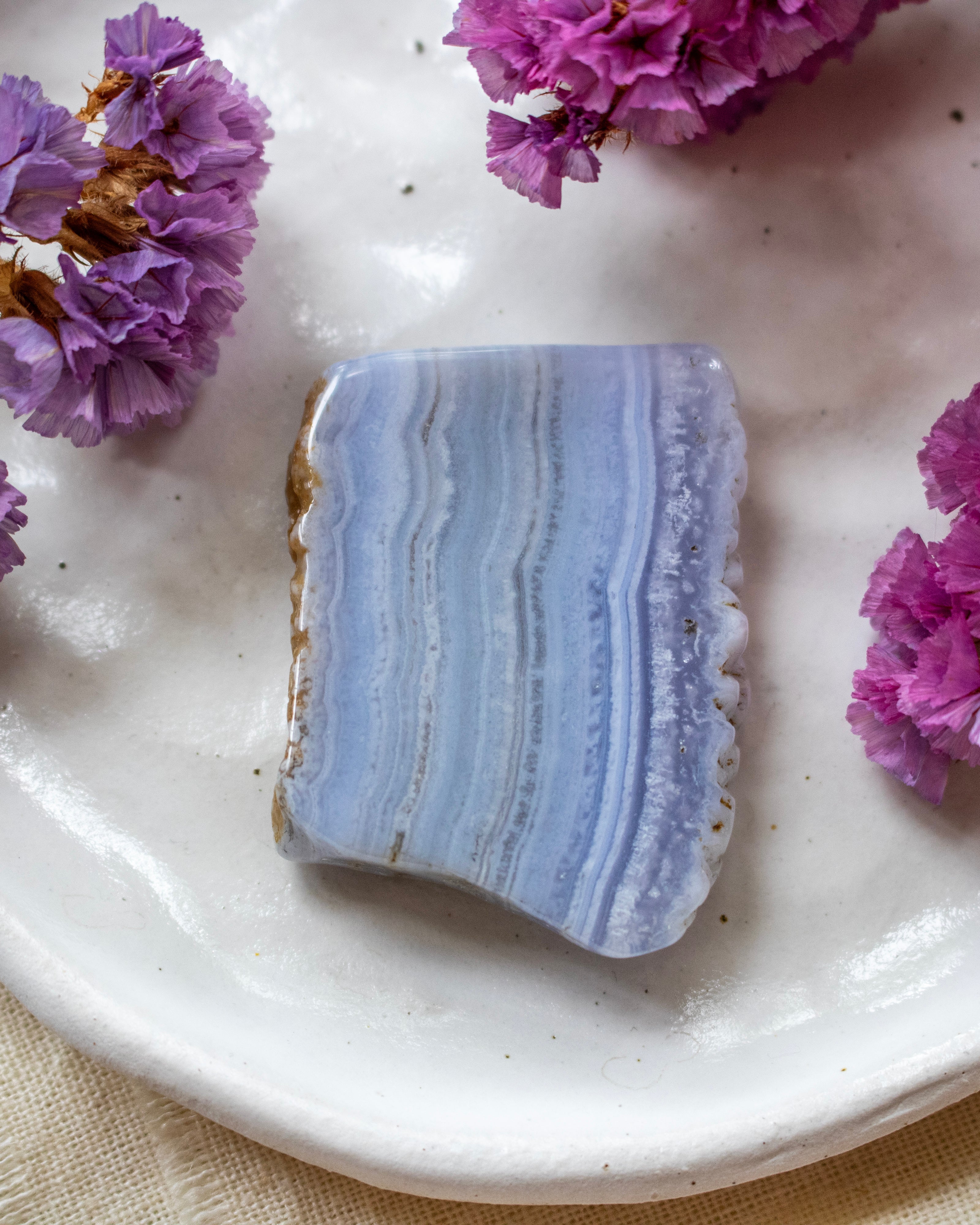 A polished rectangular stone slab with pale blue and lavender agate-like banding, placed on a white ceramic plate with purple flowers around it.