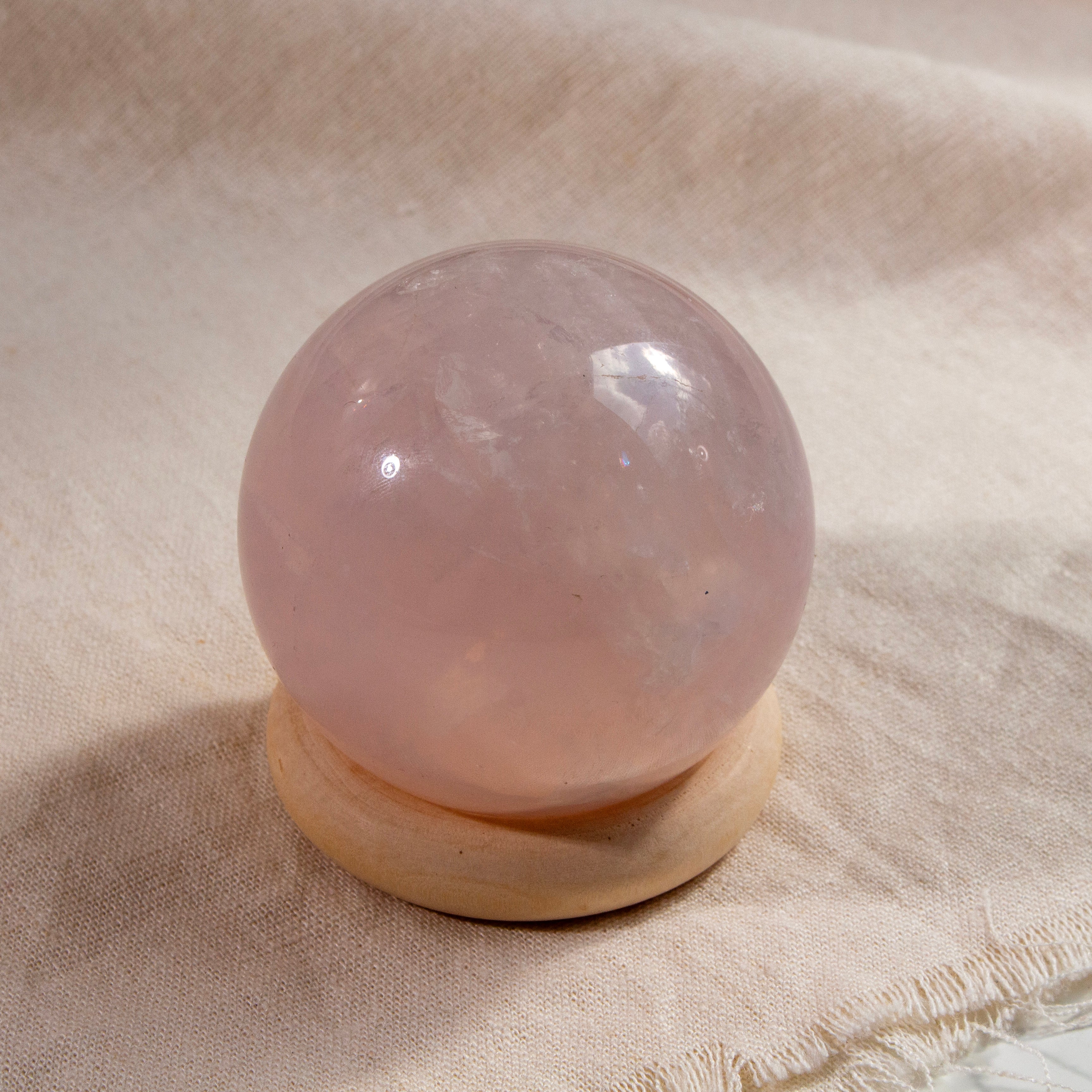 Rose quartz crystal sphere on a wooden stand against a beige fabric background