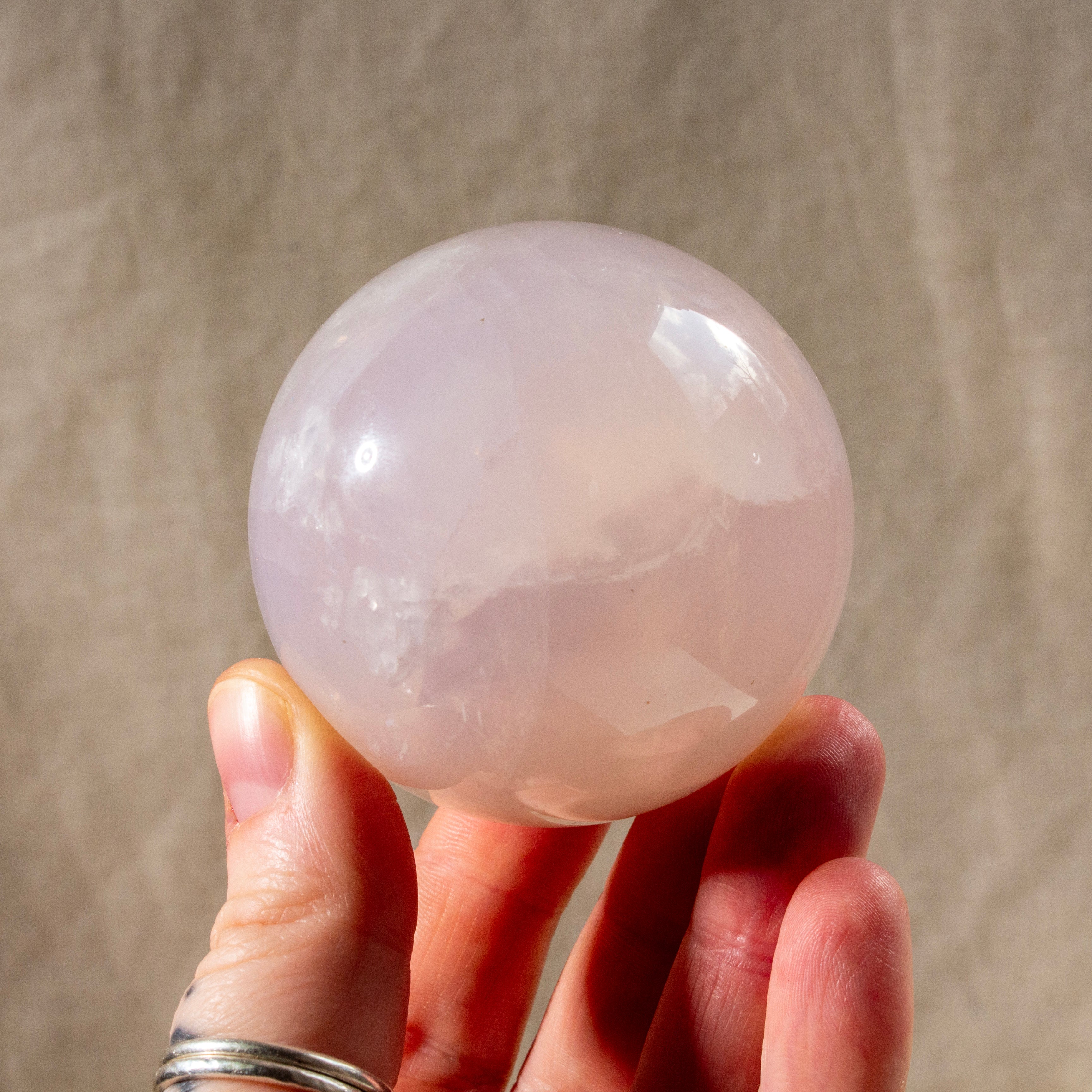 Hand holding a pink crystal ball against a neutral background