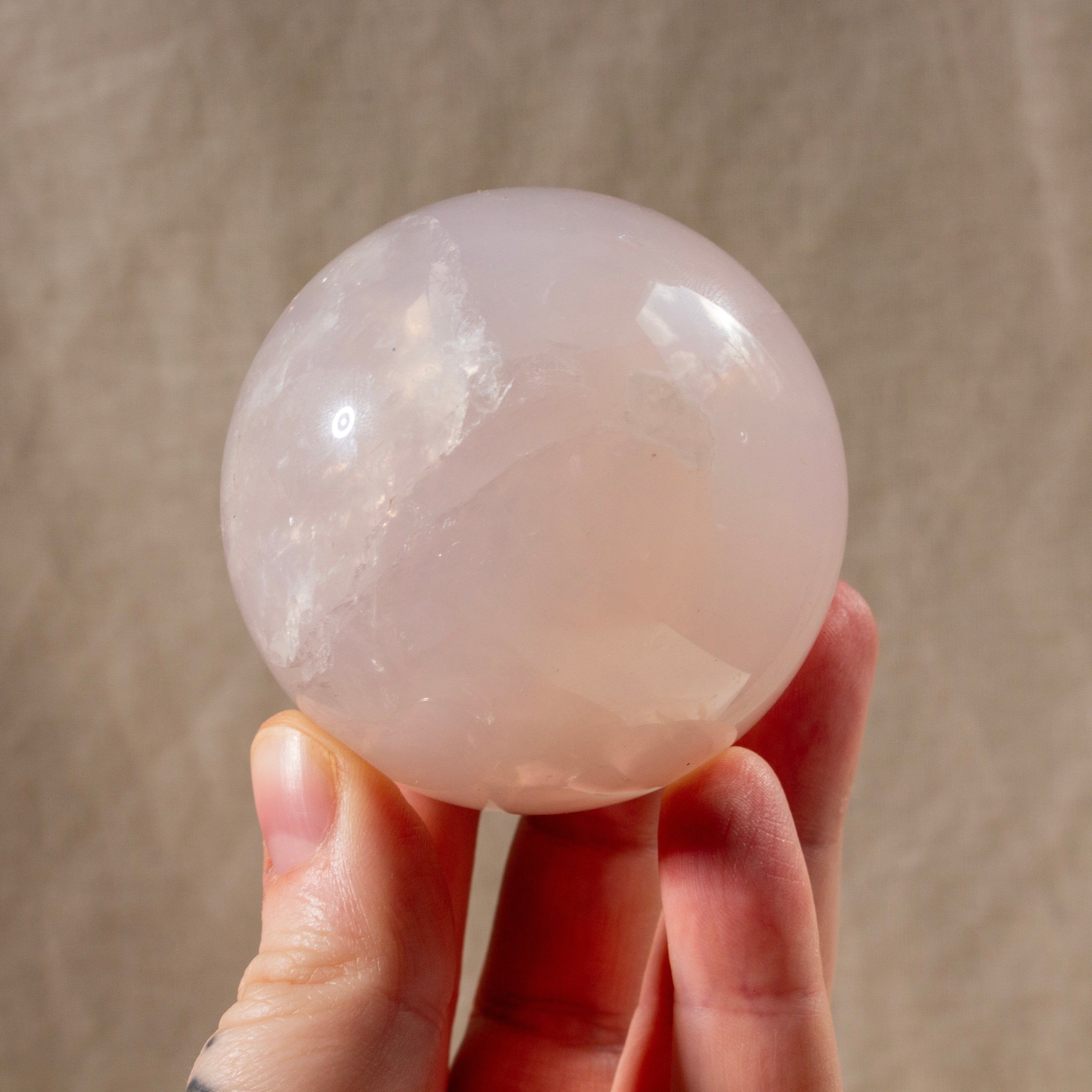 Hand holding a pink crystal sphere against a neutral background
