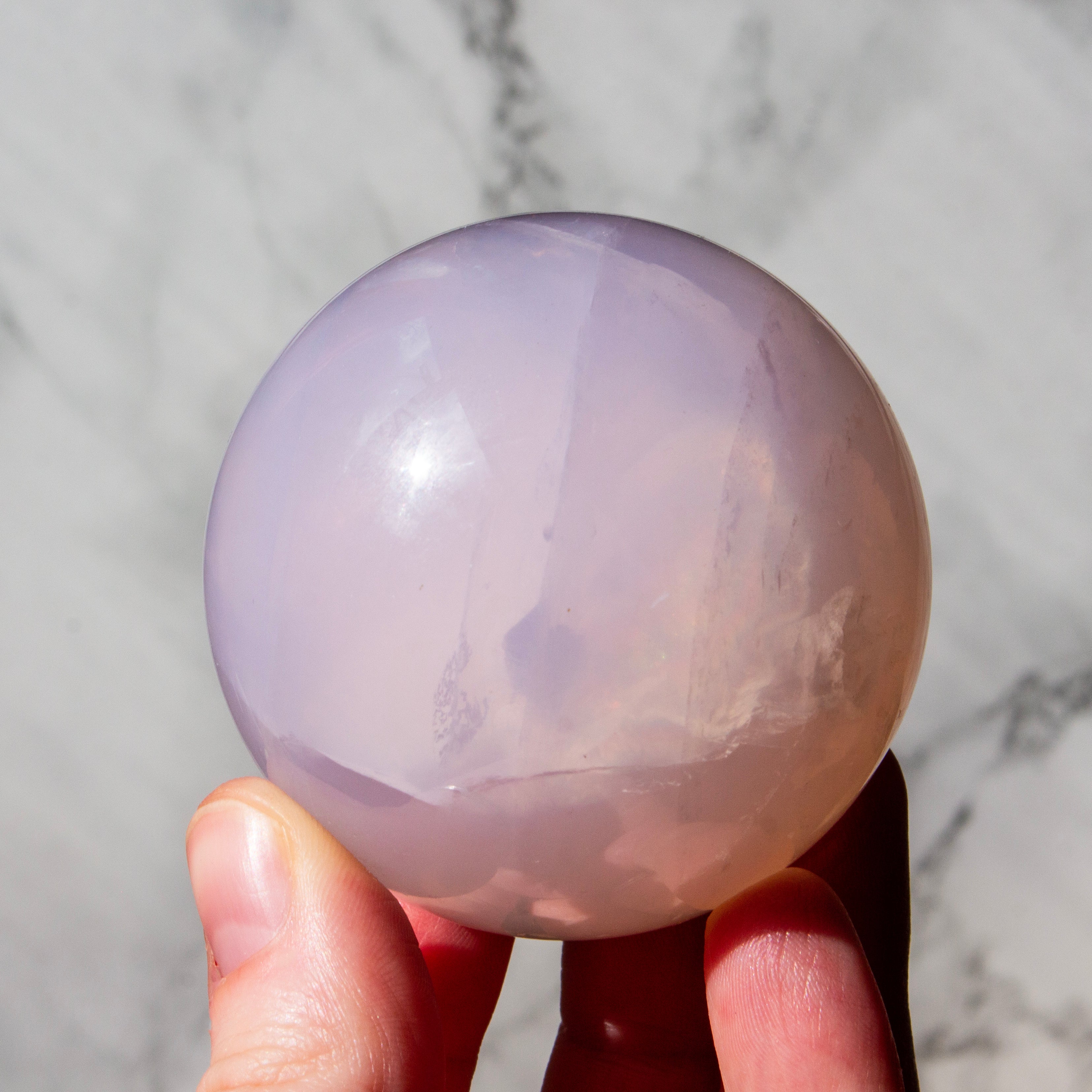 Hand holding a large, smooth, purple crystal ball against a marble background