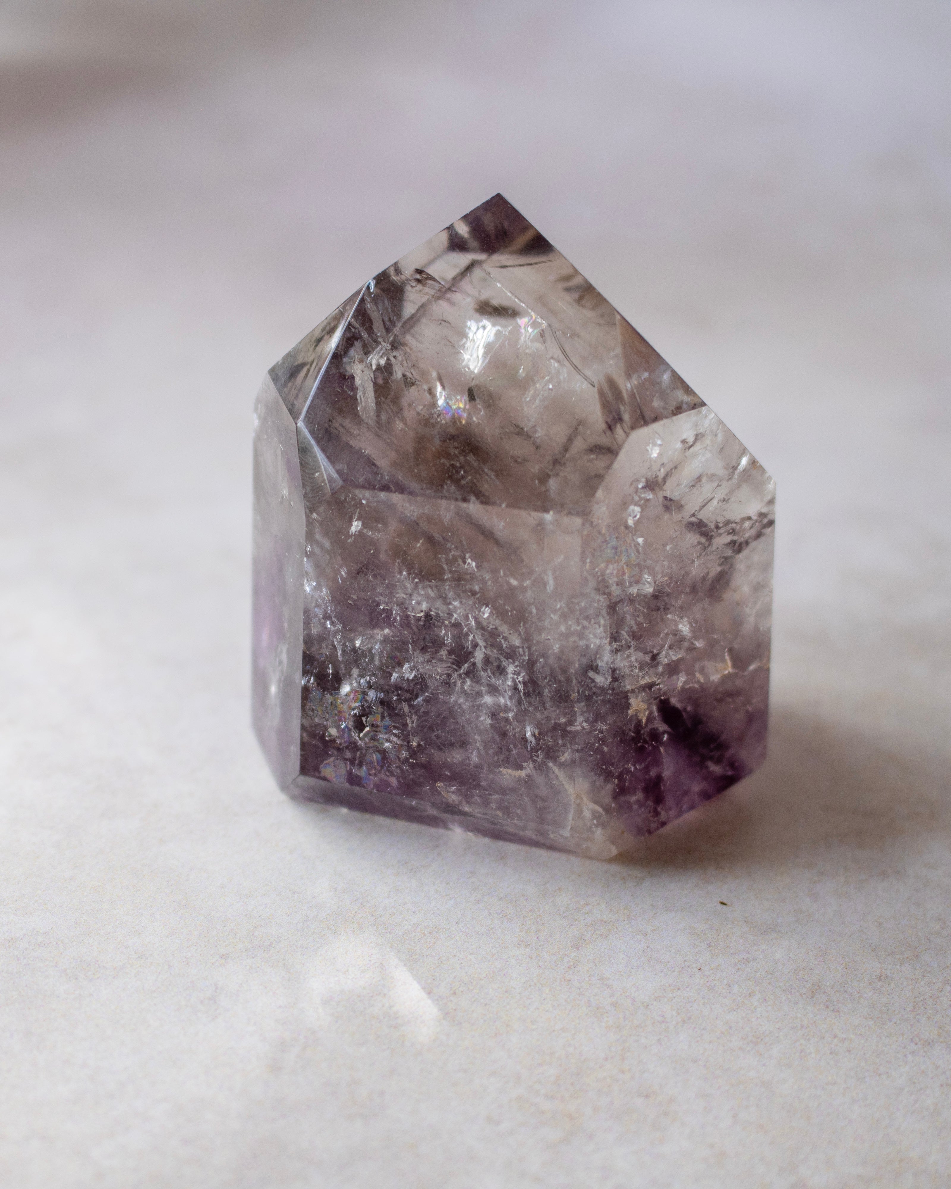 A natural pointed crystal cluster, likely amethyst, with a faceted geometric shape, resting on a light beige stone surface.
