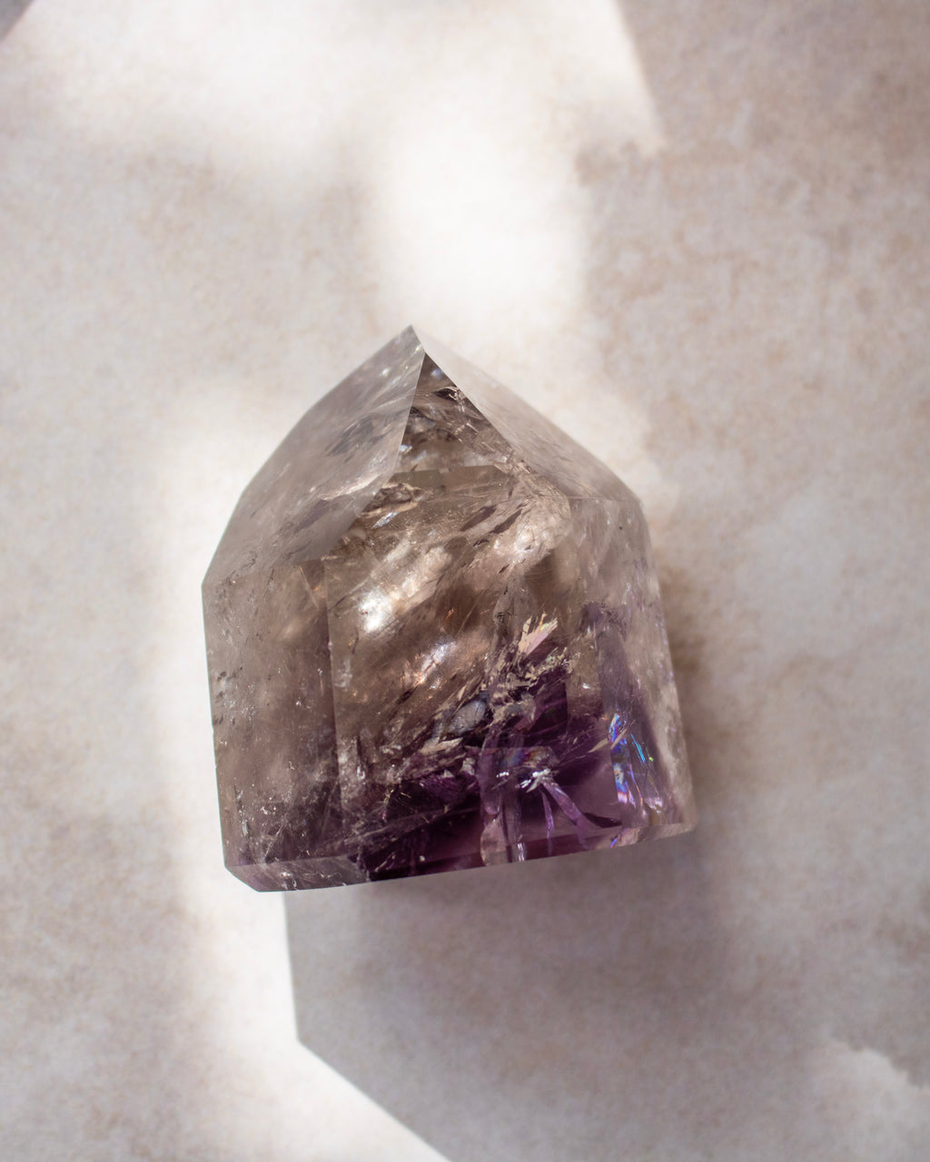 A natural amethyst crystal point with a smoky gray upper section and a deep purple base, resting on a light textured surface.