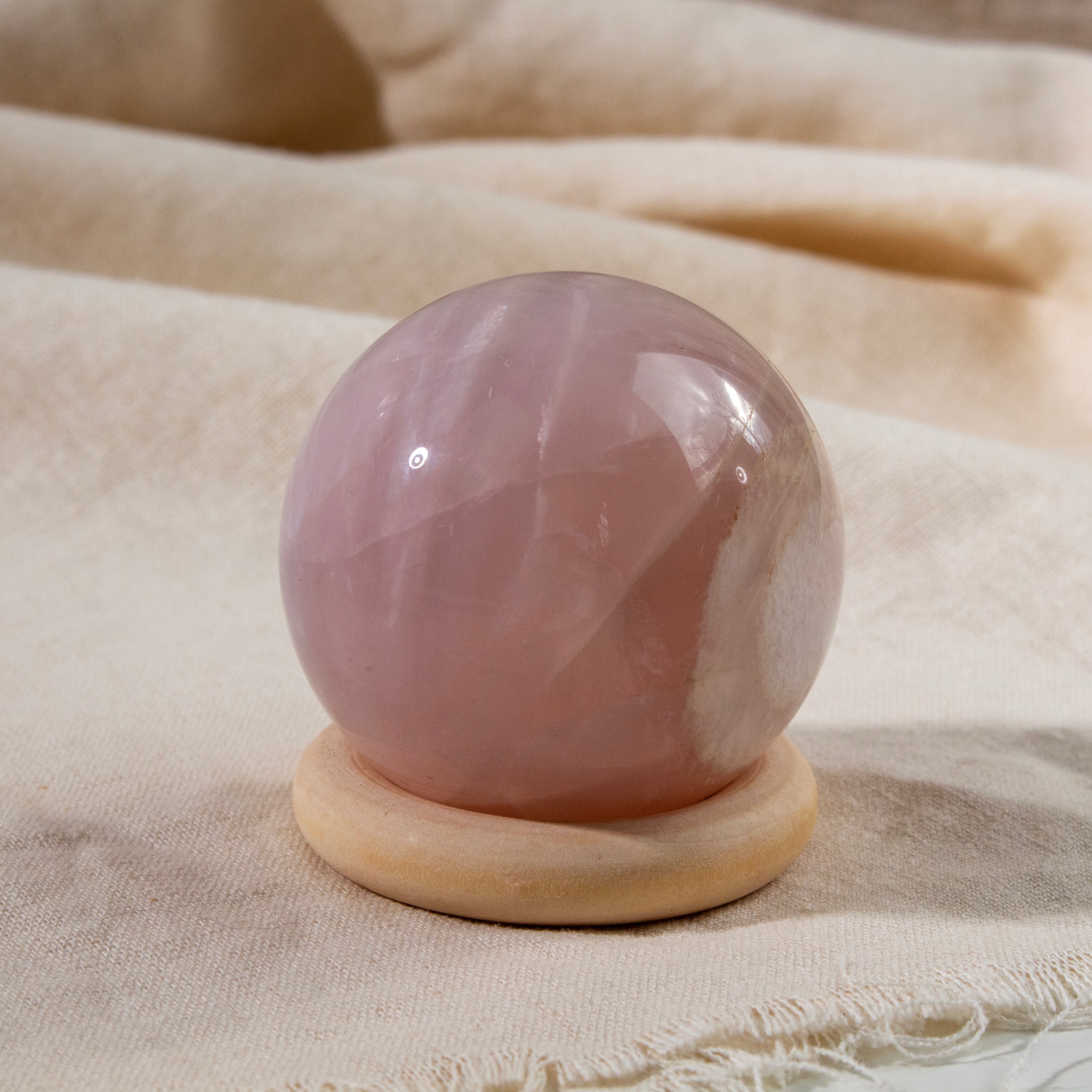 Pink crystal ball on a wooden stand with a beige fabric background