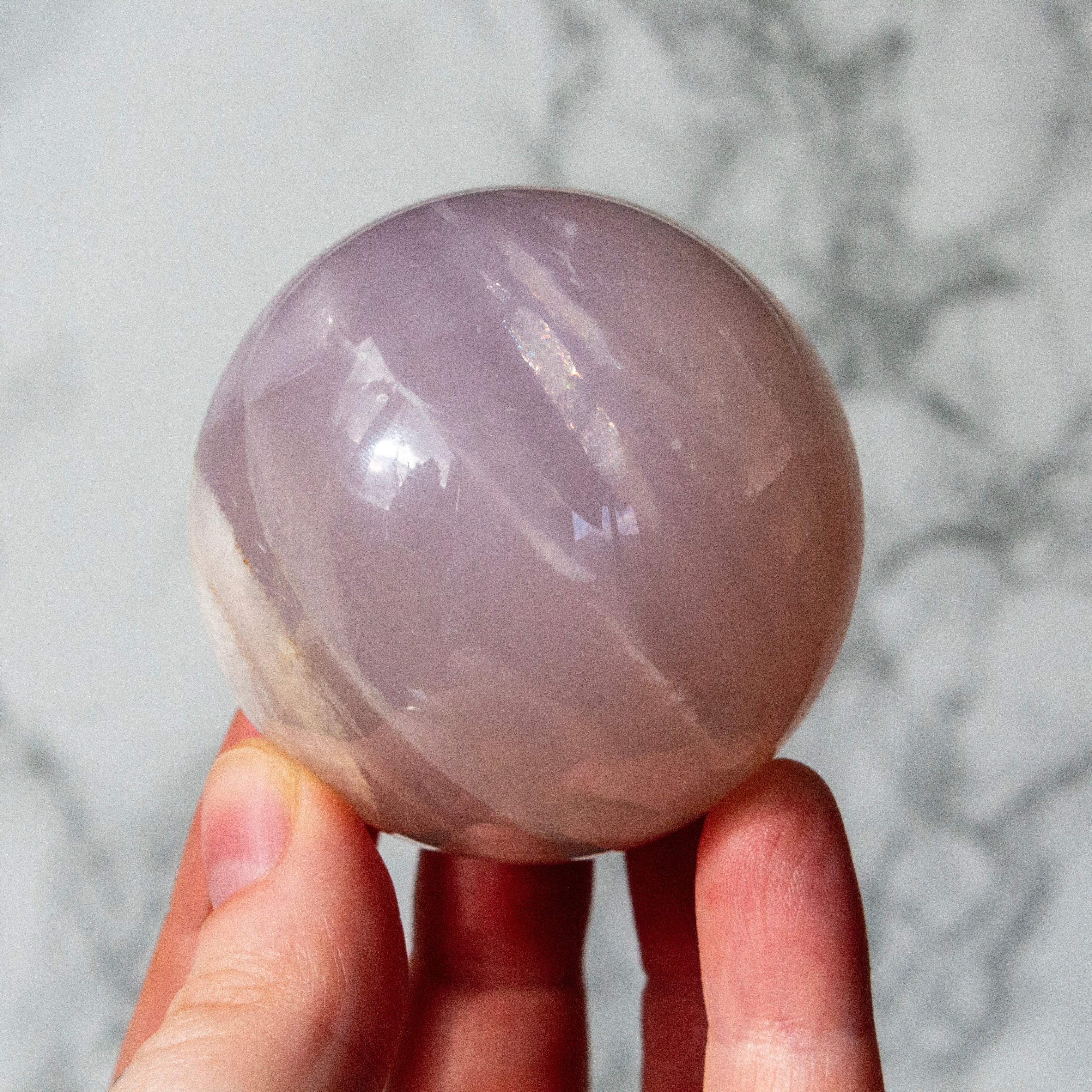 Hand holding a pink crystal ball against a marble background